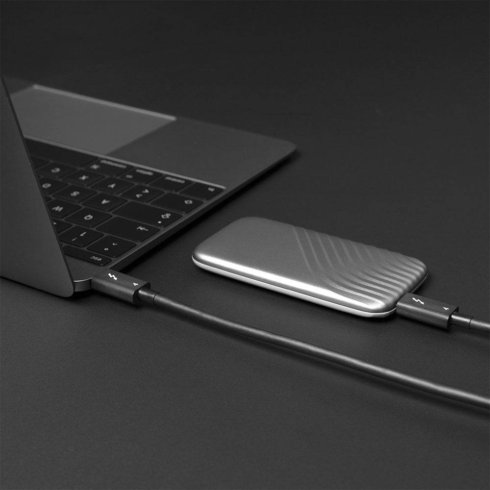 Laptop jest podłączony do zewnętrznego dysku twardego za pomocą kabla. Tło jest ciemnoszare.