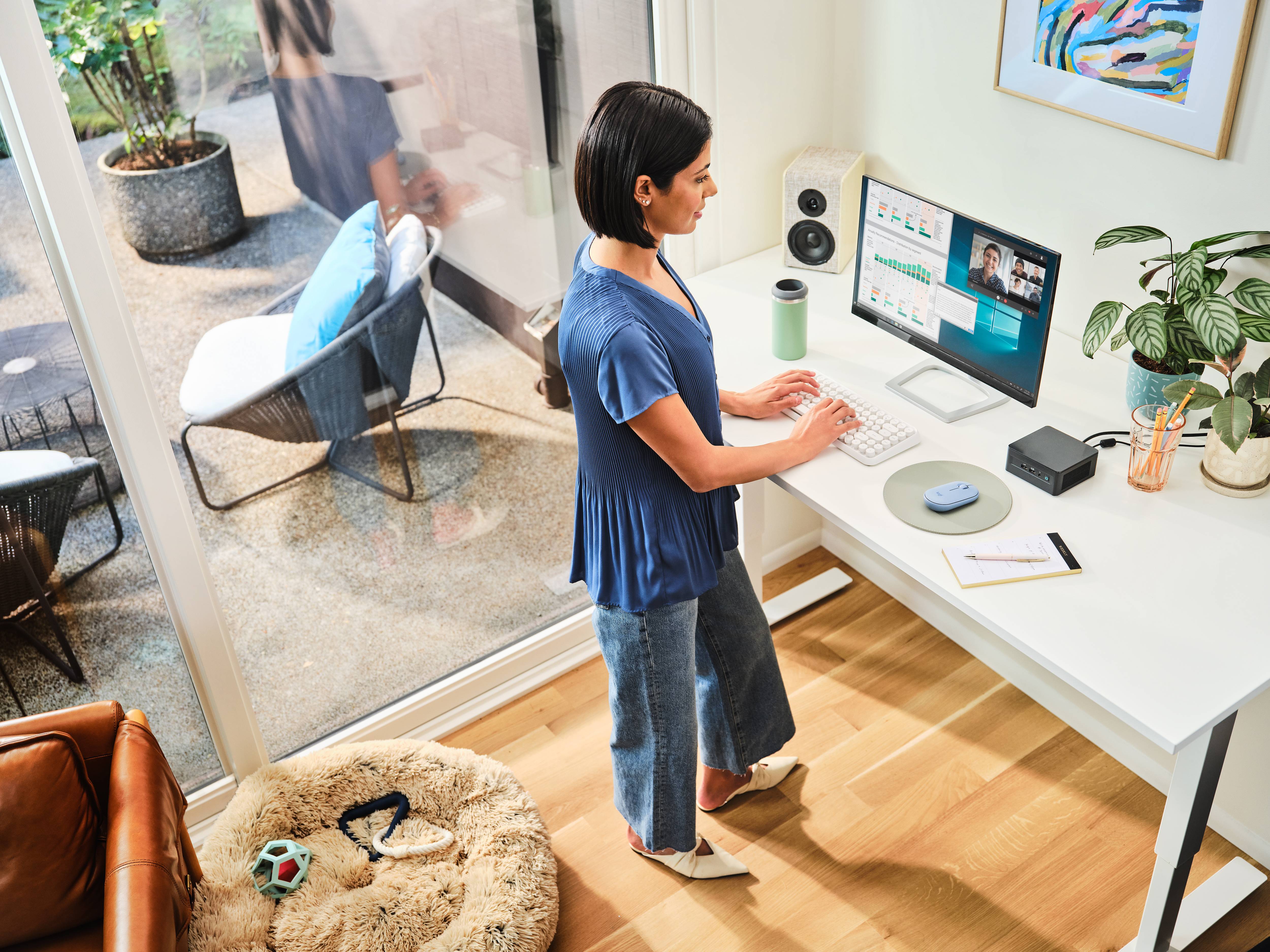 Kobieta pracuje, stojąc przy biurku z ekranem komputerowym. W tle widać jasne, przytulne pomieszczenie.