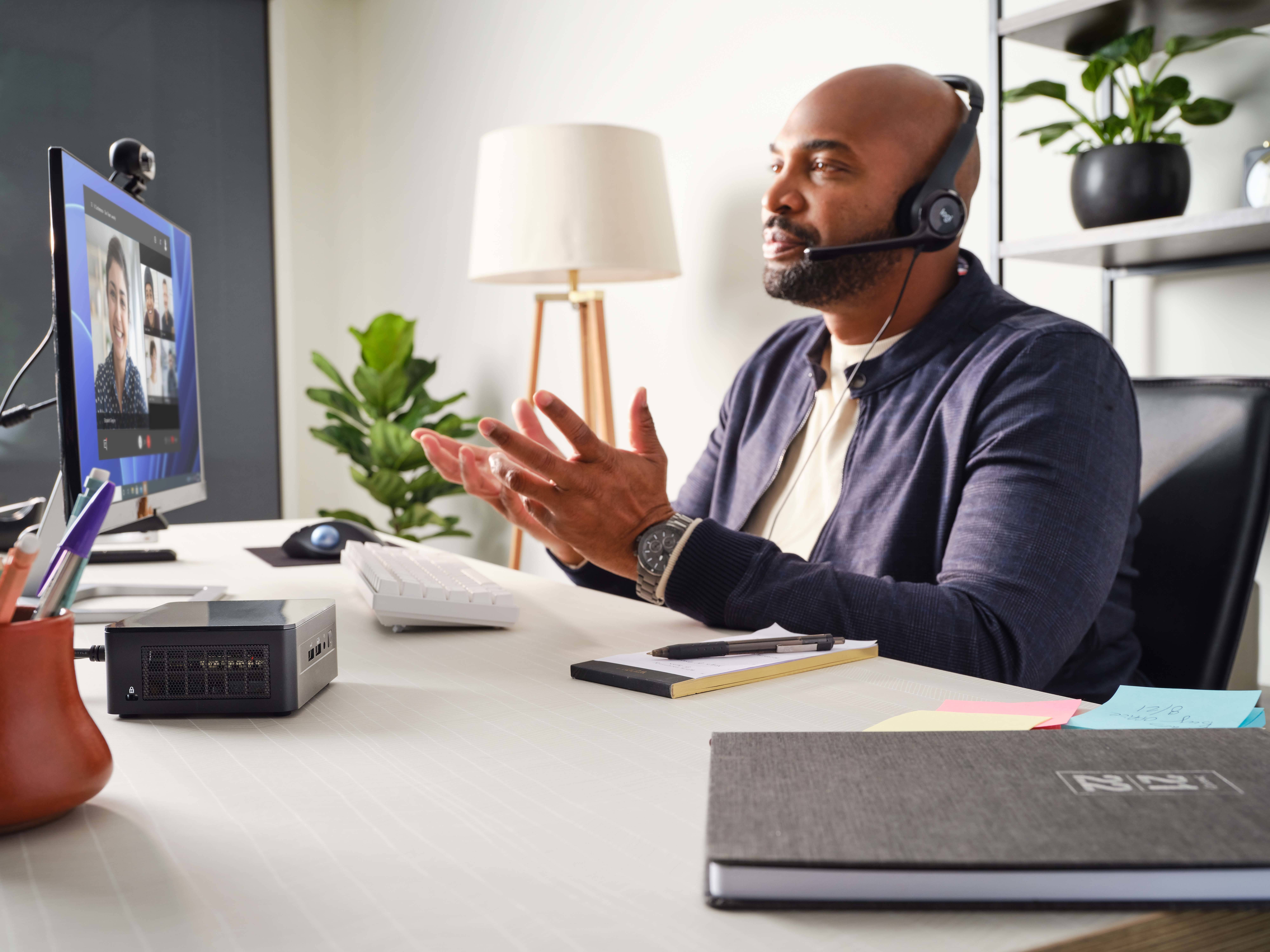 Mężczyzna w zestawie słuchawkowym siedzi przy biurku i prowadzi rozmowę wideo. W tle widać rośliny i lampę.