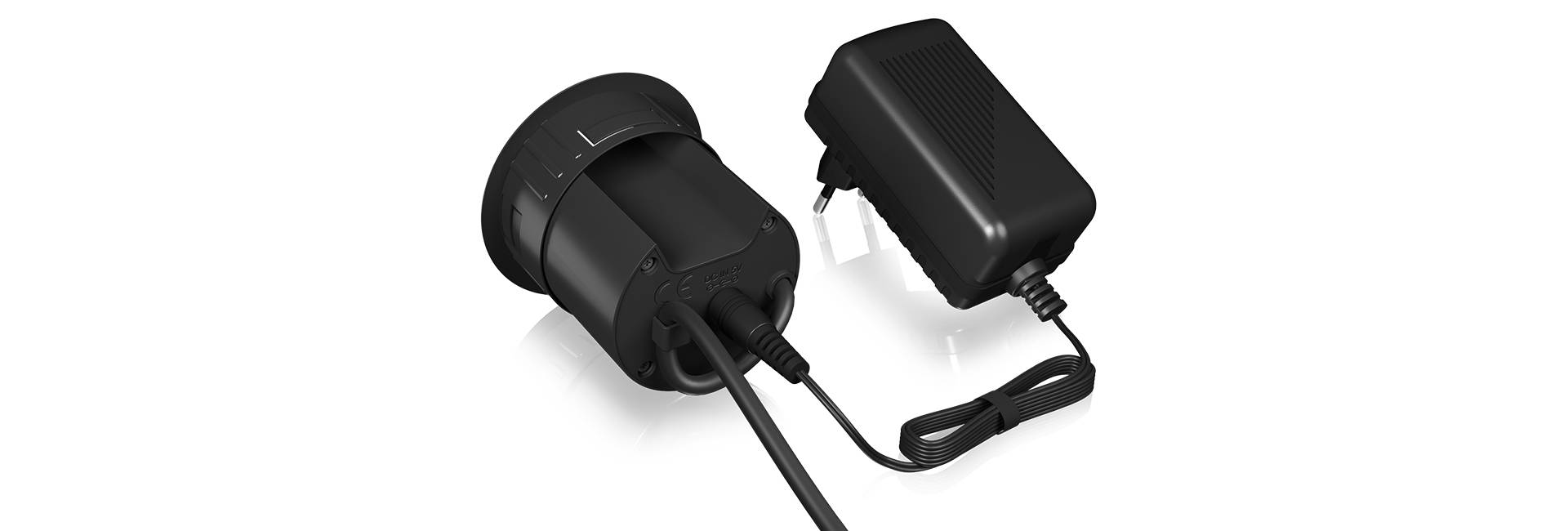 Dwa czarne urządzenia elektroniczne z przewodami, po lewej stronie adapter, po prawej ładowarka, umieszczone na białym tle.