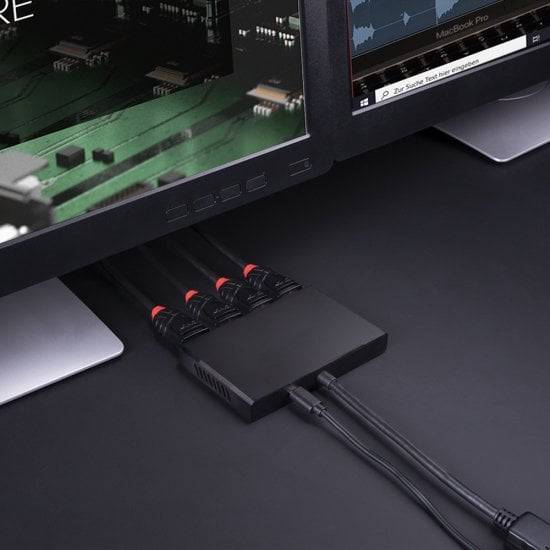 Czarny rozdzielacz HDMI łączy dwa monitory za pomocą kilku kabli HDMI na stole.