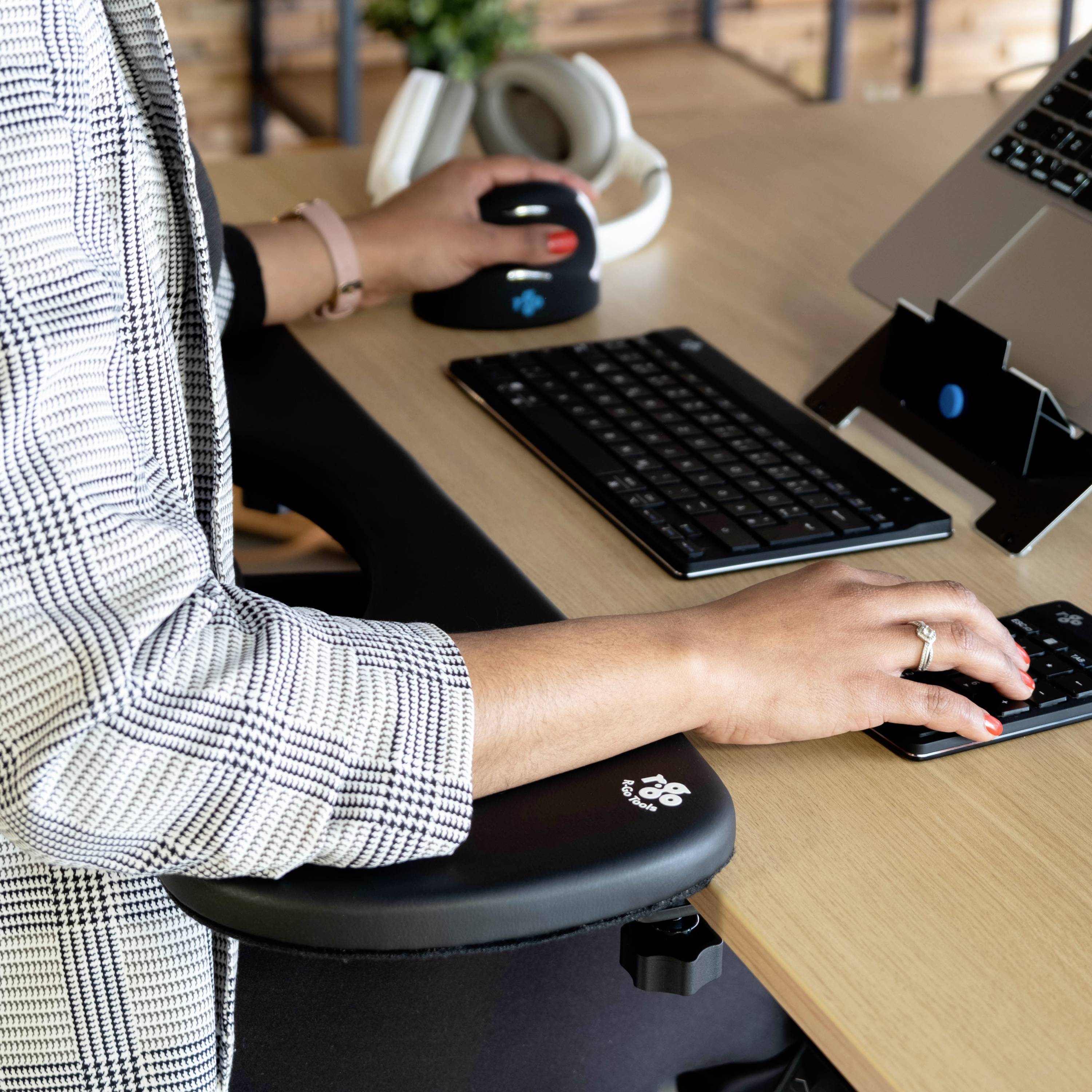 Osoba pracuje przy biurku z klawiaturą i podstawką pod laptopa. Używa ergonomicznej myszy.