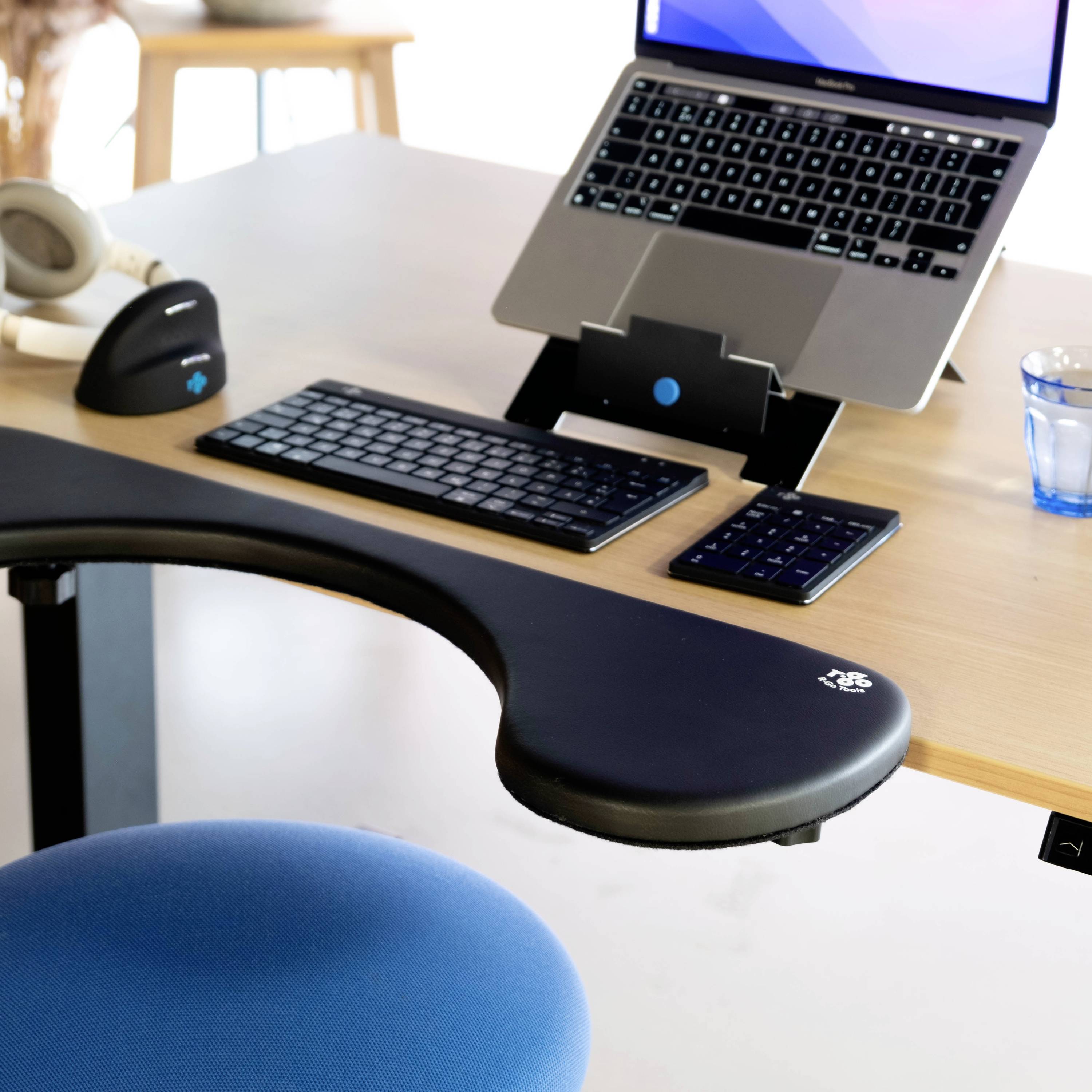 Biurko z ergonomicznym wyposażeniem, w tym laptop na podstawce, ergonomiczna klawiatura, mysz i krzesło.