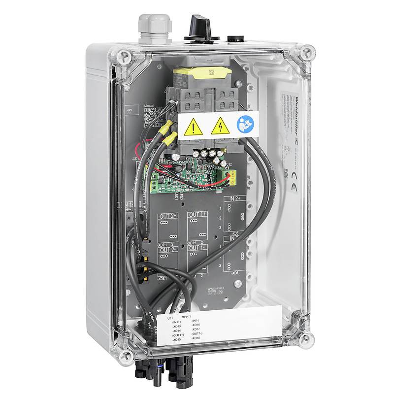 Urządzenie elektroniczne w przezroczystej obudowie z wieloma przewodami i obwodami. Na powierzchni widoczne są naklejki z symbolami ostrzegawczymi.