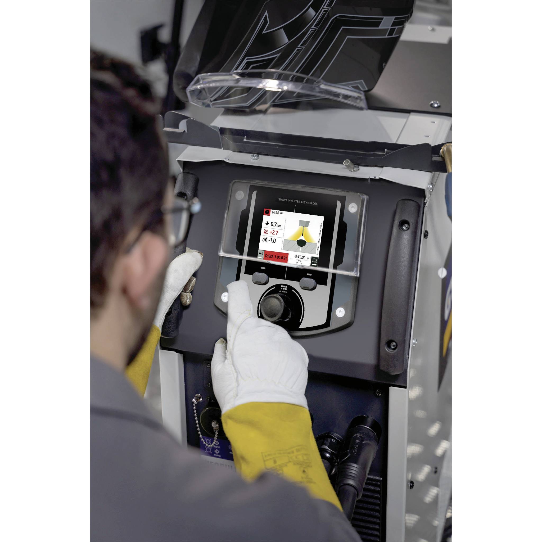 Mężczyzna obsługuje spawarkę, patrząc na wyświetlacz z różnymi ustawieniami. Ma na sobie rękawice ochronne i okulary ochronne.