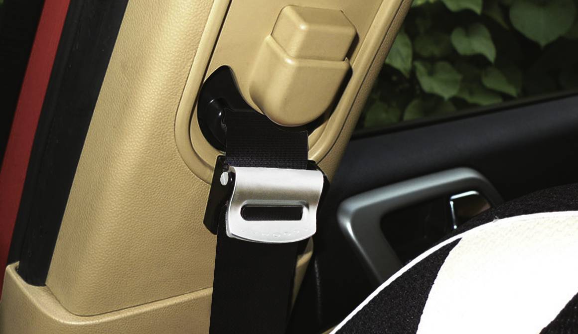 Pas bezpieczeństwa jest zamocowany przy słupie samochodu, obok siedzenia w czarno-białym wzorze. W tle widoczne są zielone liście.