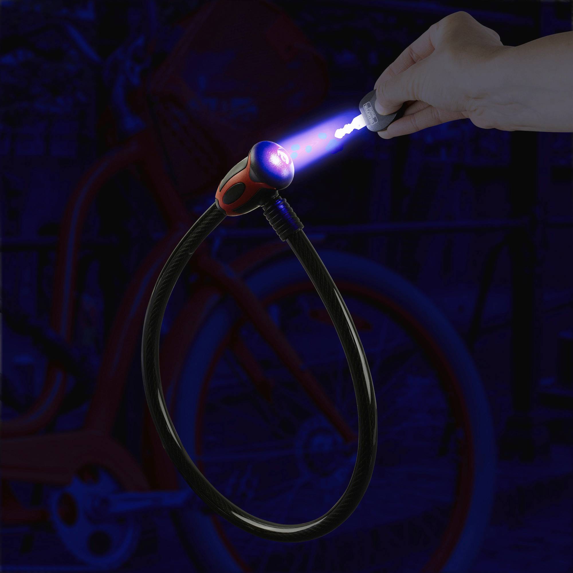 Dłoń naciska świecący przycisk na zamku rowerowym, który rozbłyska w ciemności. W tle widoczny jest rower.