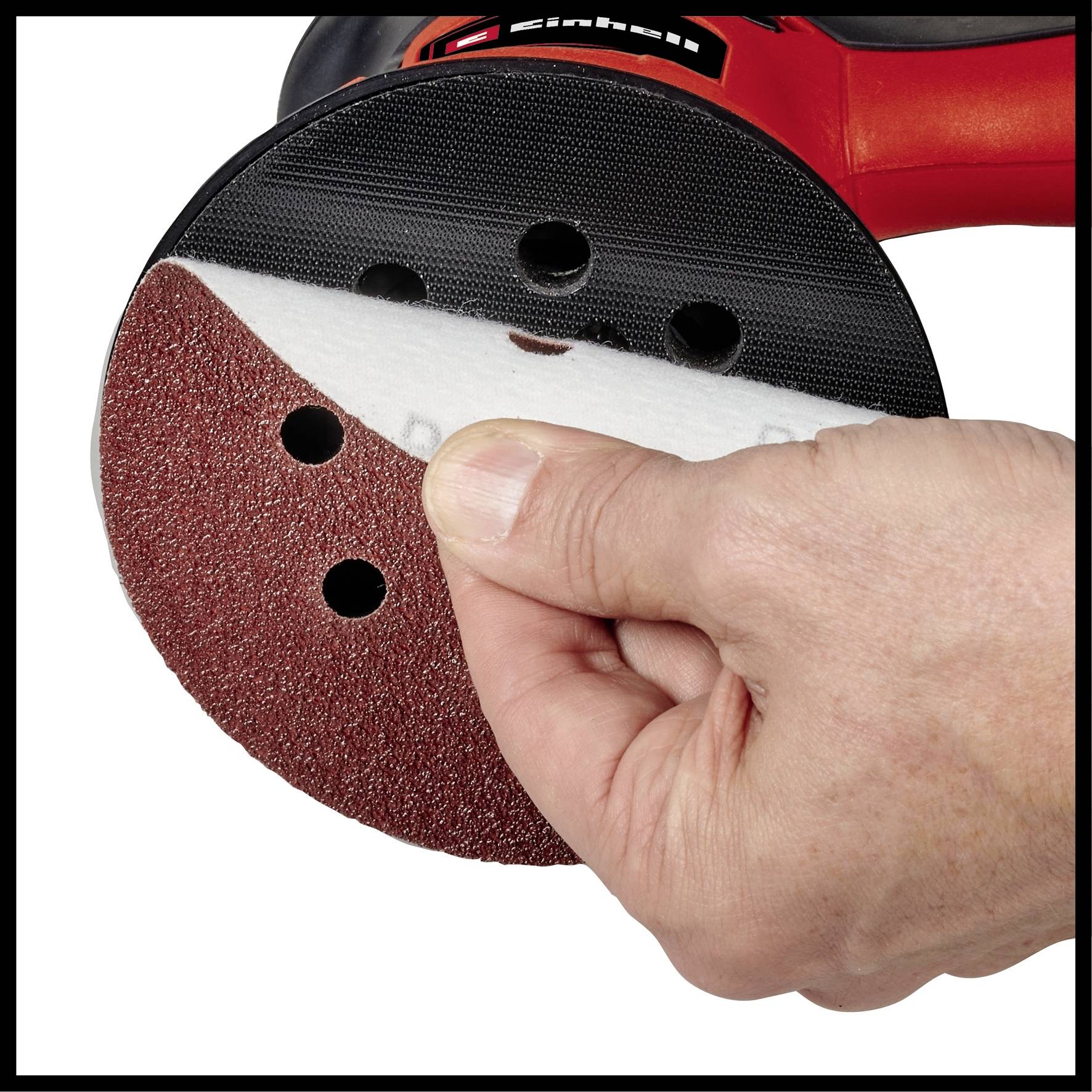 Dłoń przykleja okrągły papier ścierny z otworami na czerwoną szlifierkę. Narzędzie nadaje się do szlifowania powierzchni.