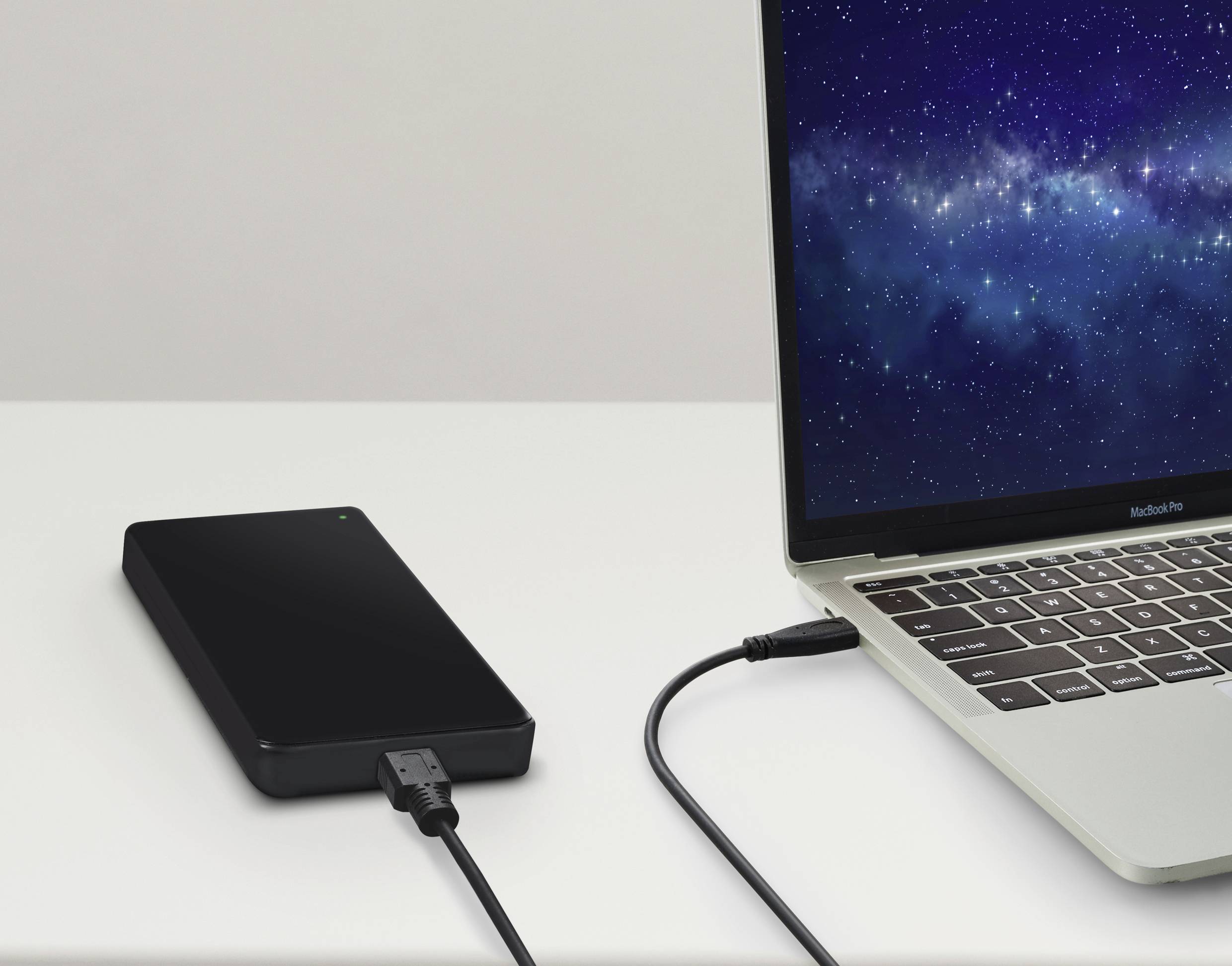 Zewnętrzny dysk twardy podłączony do laptopa na stole. Laptop wyświetla tapetę z gwiaździstym niebem.