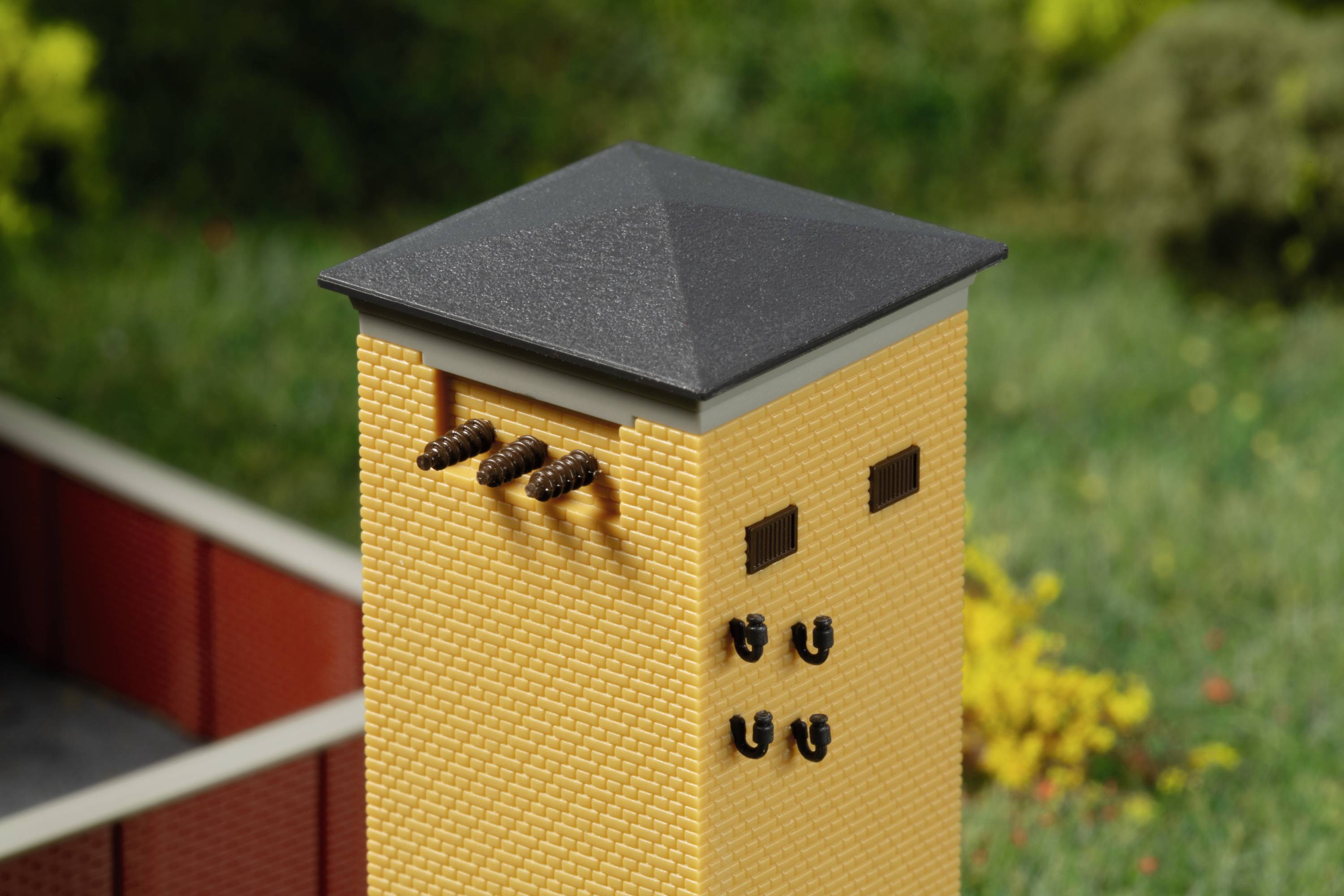 Żółty budynek z ciemnym dachem i kilkoma małymi otworami po bokach, otoczony zieloną scenerią w tle.