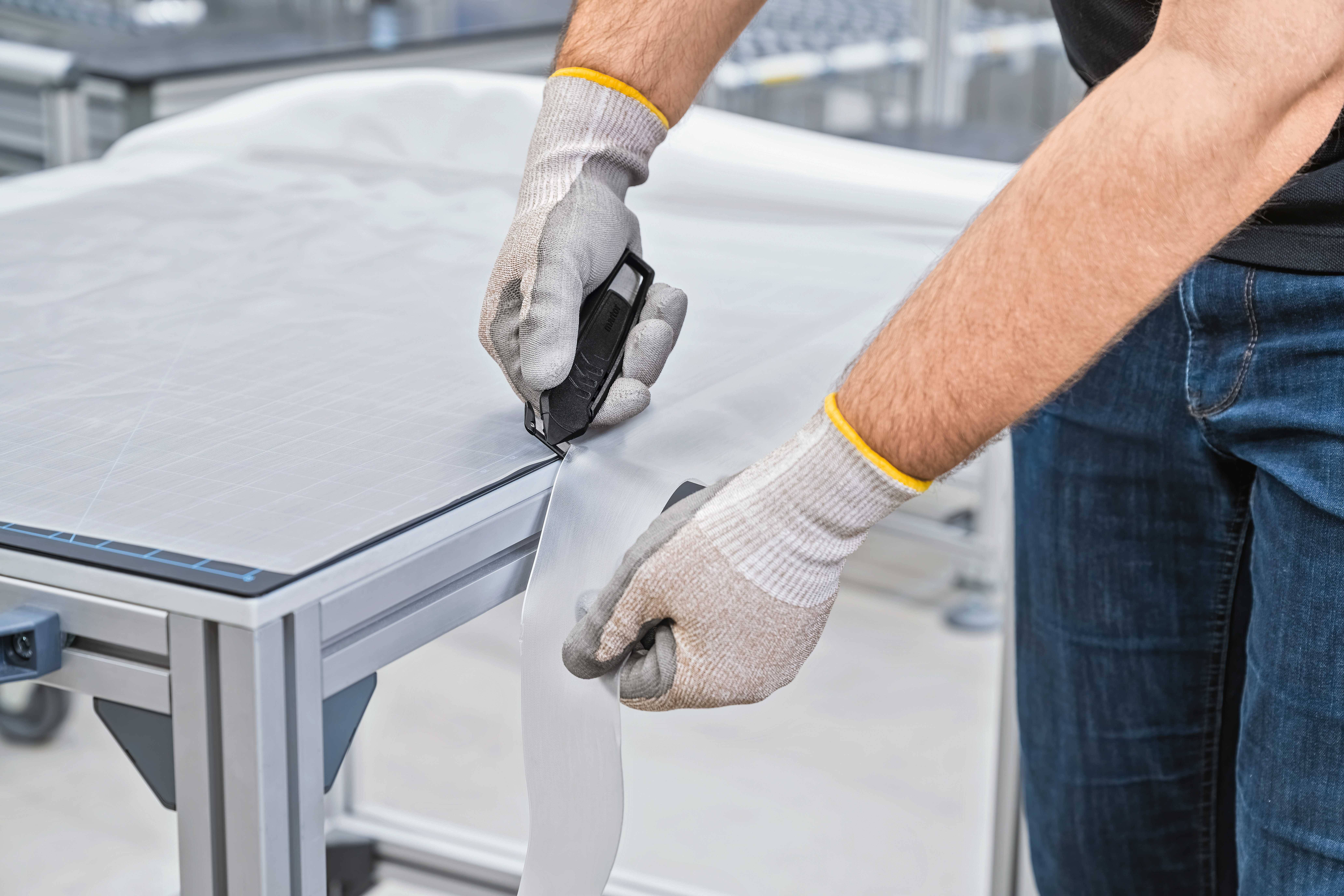 Osoba w rękawiczkach przycina białą substancję na stole nożem monterskim.