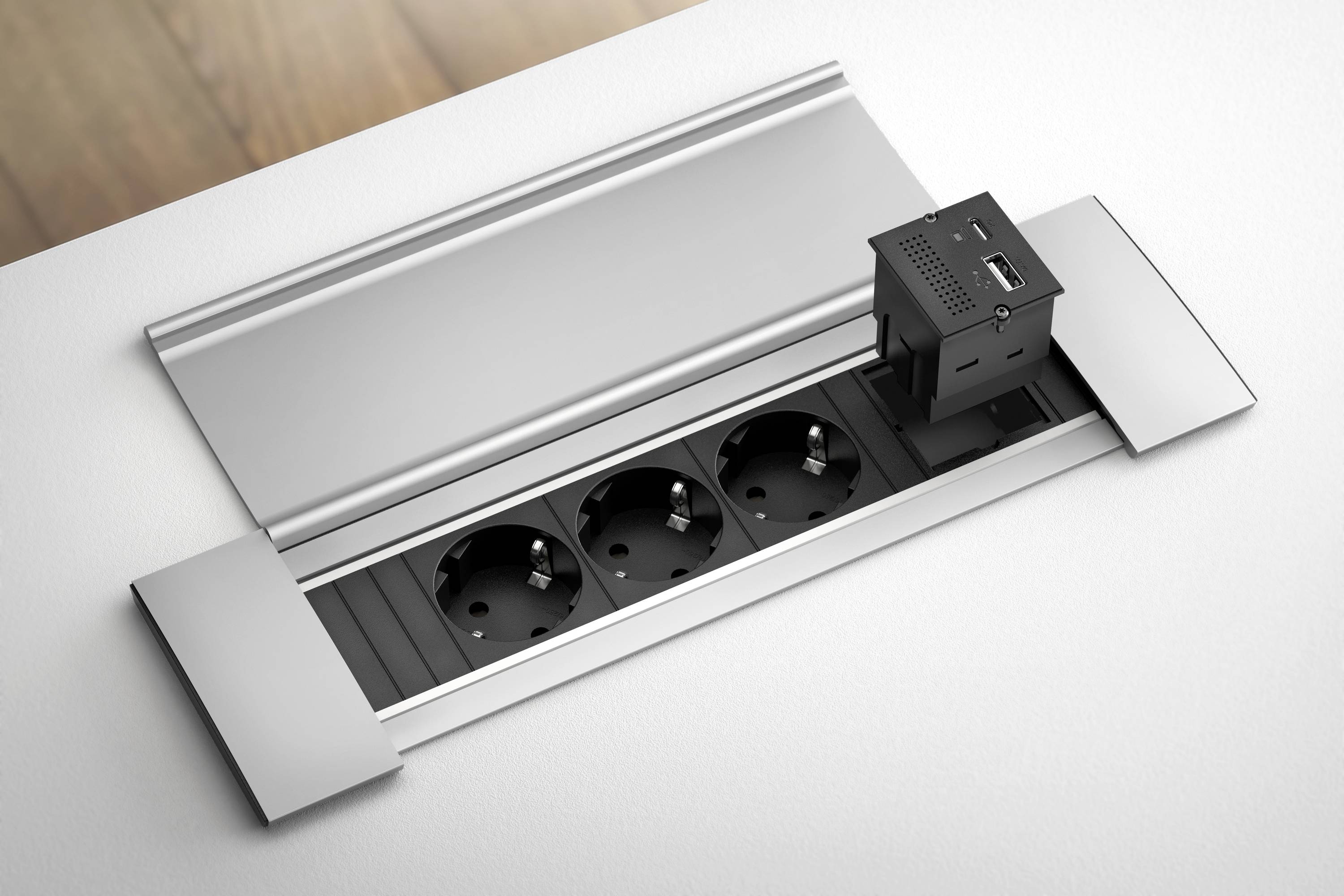 Przedłużacz do blatu z trzema gniazdami elektrycznymi i zintegrowanym portem USB, dyskretnie wmontowany w powierzchnię roboczą.