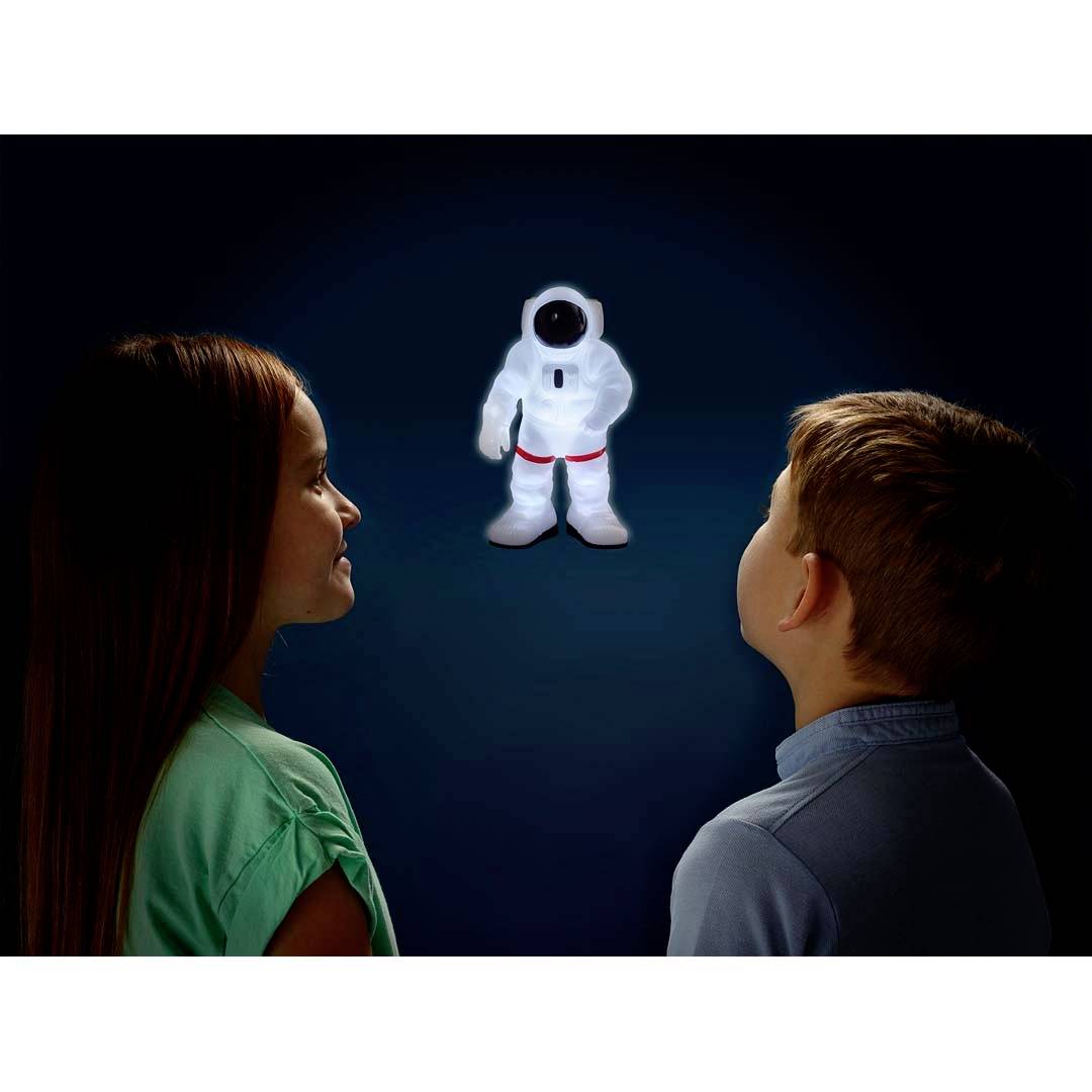 Dwoje dzieci z zaciekawieniem przygląda się świecącej figurce astronauty na ciemnym tle.