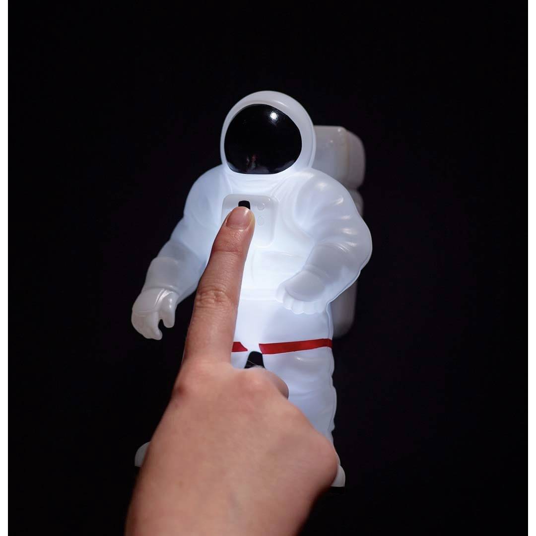Dłoń dotyka świecącej postaci astronauty w ciemności. Postać ma na sobie biały kombinezon z czerwonym pasem.