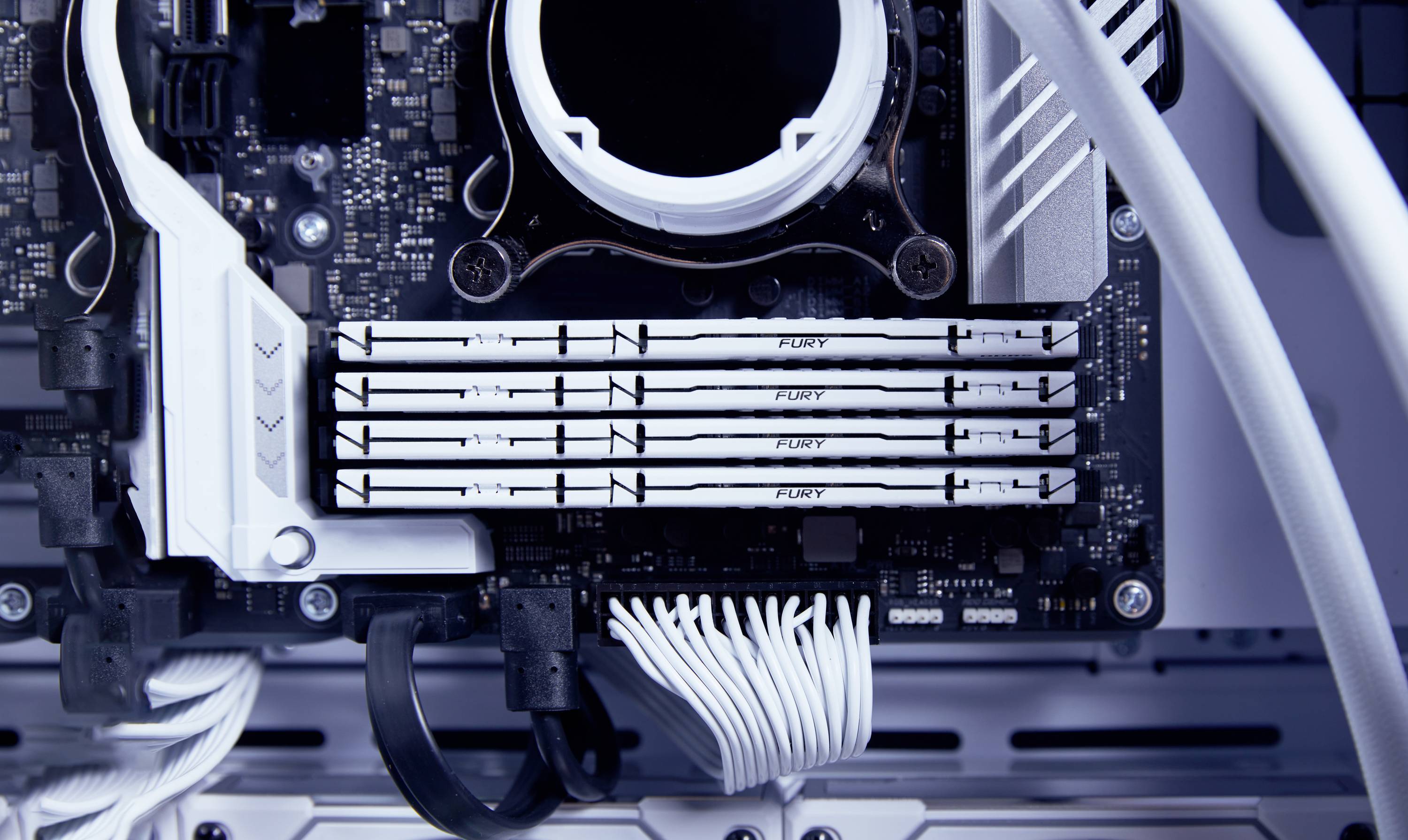 Zbliżenie płyty głównej komputera z zainstalowanymi modułami RAM i białymi kablami, prezentujące komponenty technologiczne.