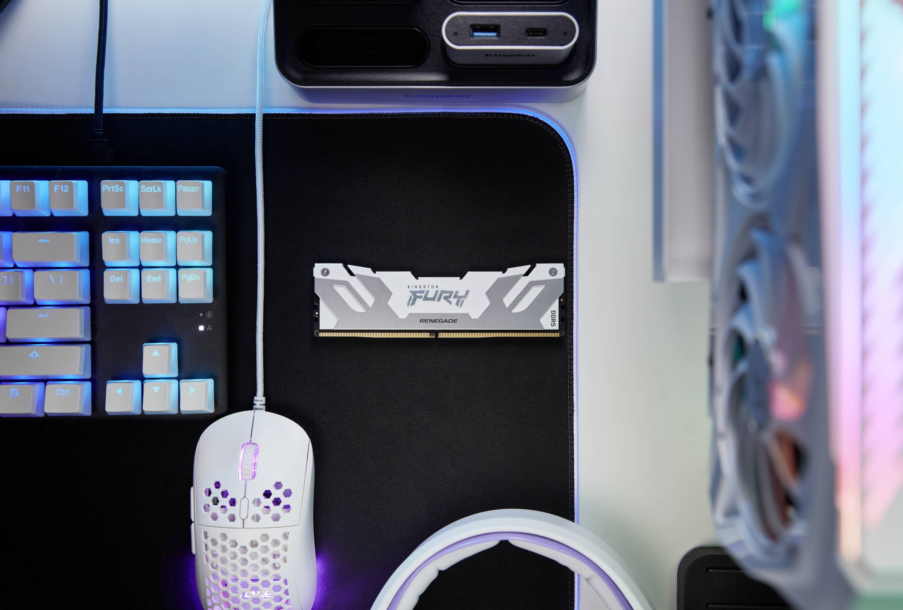 Klawiatura komputerowa, mysz i moduł RAM na biurku, otoczone świecącymi diodami LED. Kolory zmieniają się między niebieskim a fioletowym.