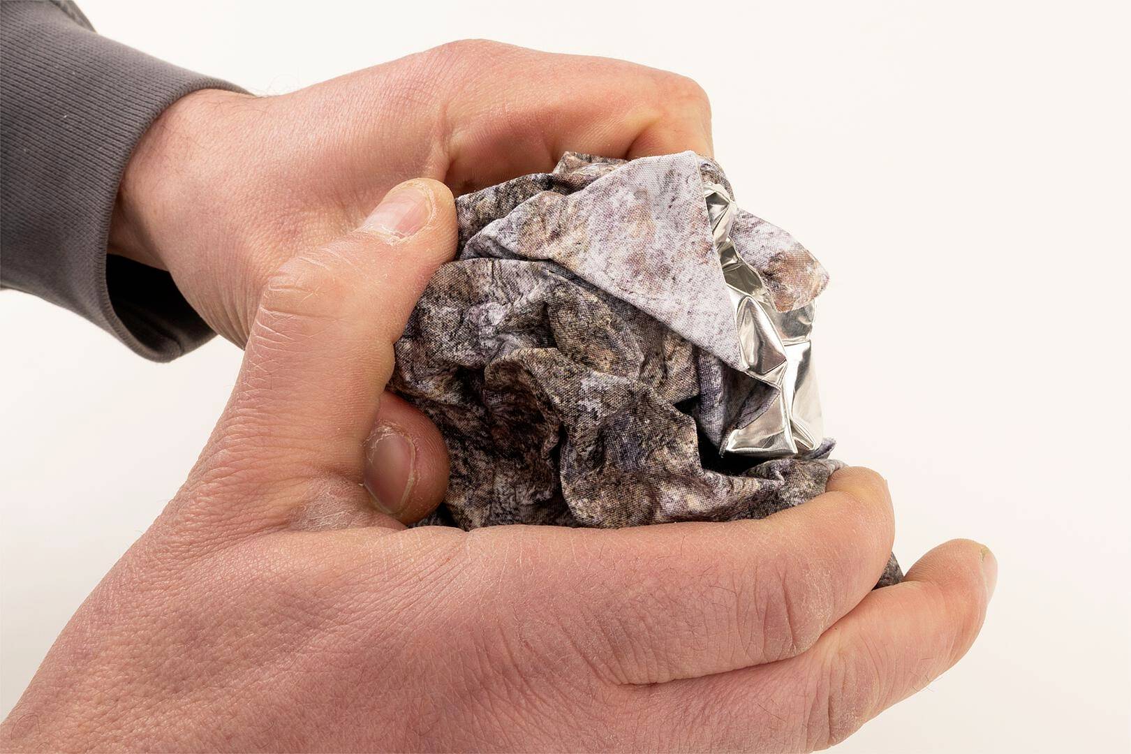 Dwie ręce miażdżą pozgniatany papier, formując go w kulę.