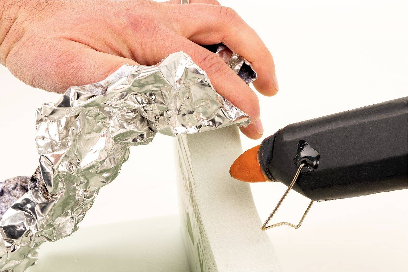 Osoba pracuje z pistoletem do kleju na gorąco i formuje folię aluminiową wokół obiektu.