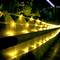 Żółte lampki choinkowe świecą się na drewnianej balustradzie nocą, otoczone roślinami, tworząc przytulną atmosferę.