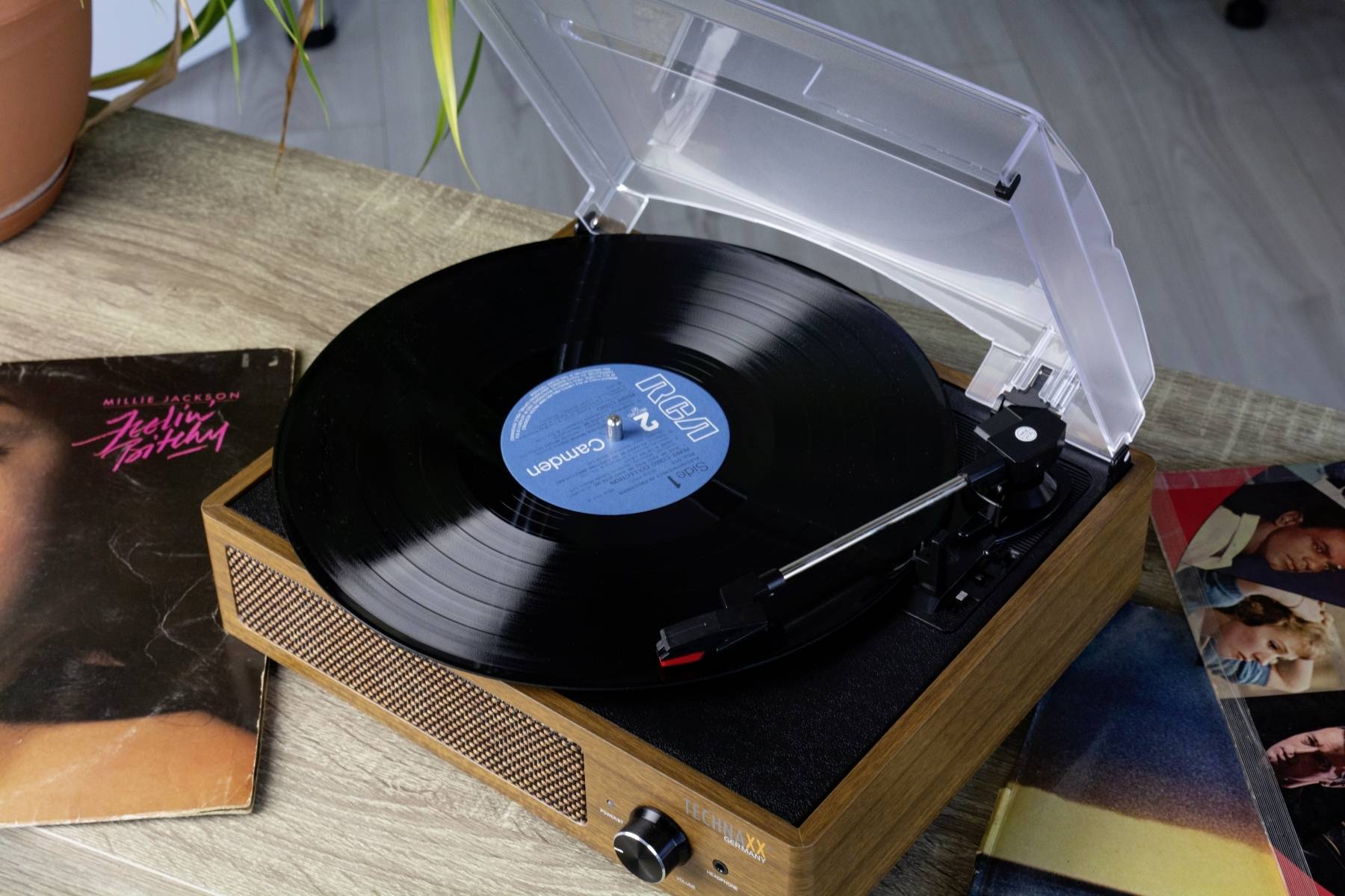 Gramofon odtwarza płytę winylową na drewnianym stole. Obok leżą dwie okładki płyt.