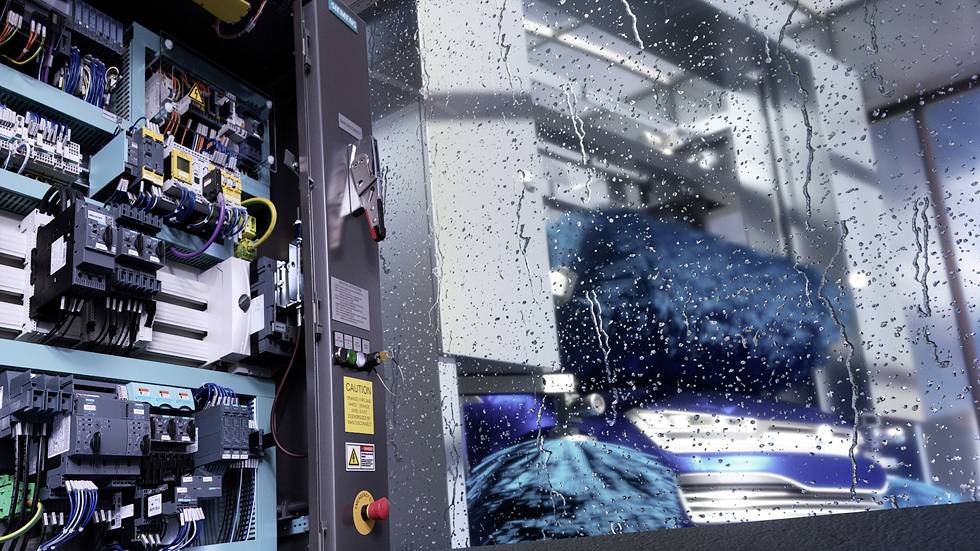 Otwarty rozdzielnik elektryczny ujawnia techniczne komponenty, podczas gdy maszyna pracuje za przezroczystym, mokrym od deszczu oknem.