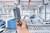 Ręka trzyma urządzenie elektroniczne w dużym, zautomatyzowanym zakładzie przemysłowym. W tle widoczne są przenośniki taśmowe.
