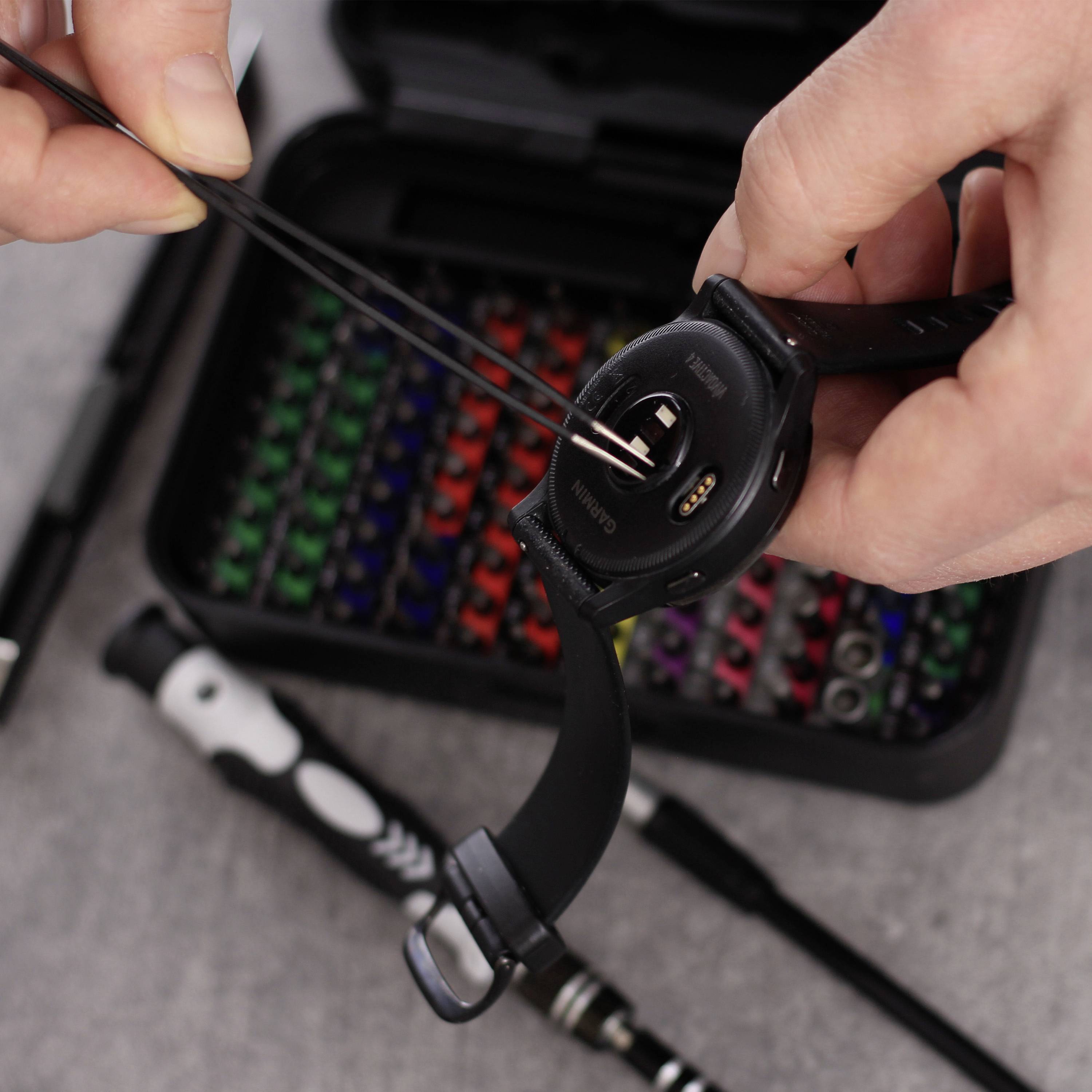 Osoba zdejmuje gumkę od smartwatcha, w tle narzędzia; fokus na zdejmowaniu opaski.