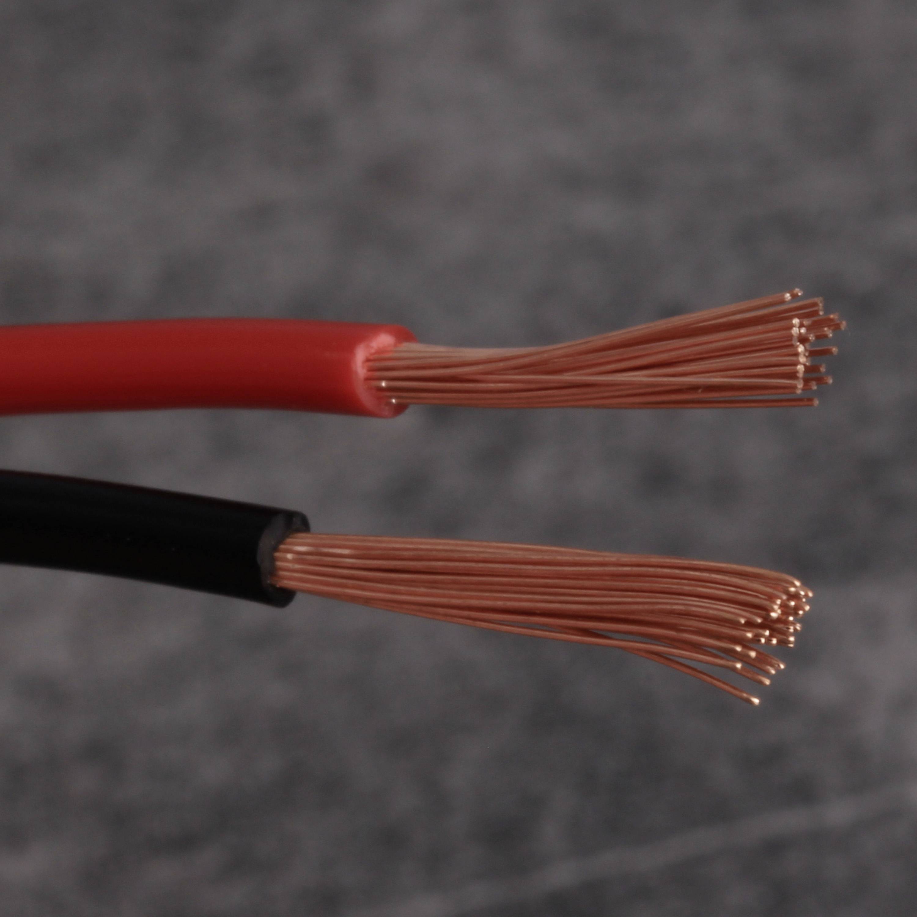 Czerwone i czarne przewody elektryczne z odkrytymi przewodami miedzianymi, leżące obok siebie na szarym tle.