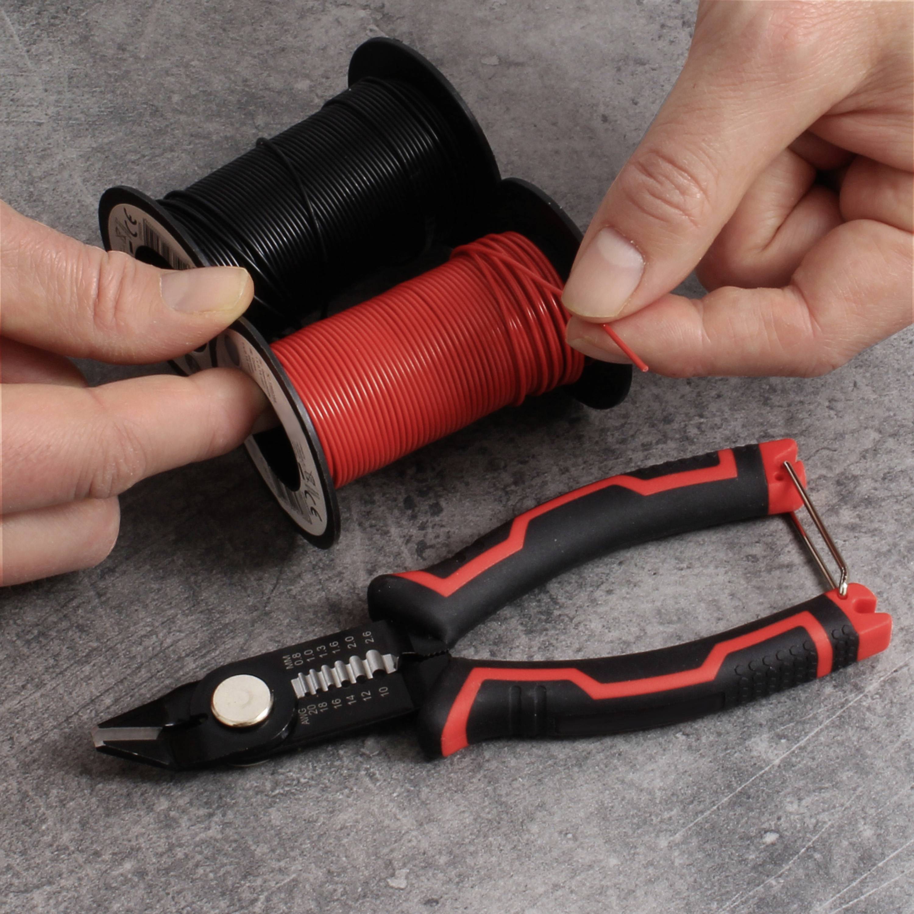 Dwie ręce trzymają rolki czerwonego i czarnego kabla, obok leżą szczypce na szarym stole.