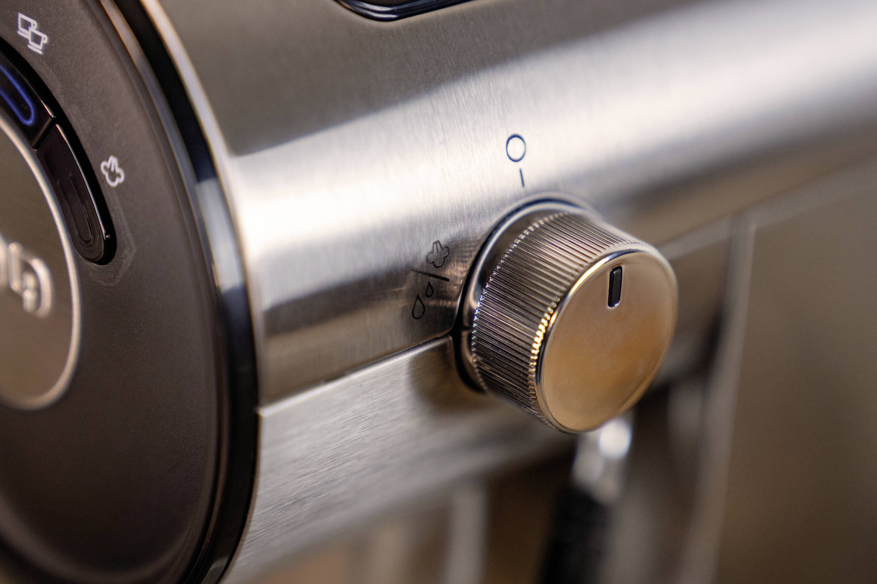 Lśniący metalowy przycisk na urządzeniu elektrycznym, z oznaczeniami ustawień włączania i wyłączania. Obok przycisku widoczne są dodatkowe przyciski.