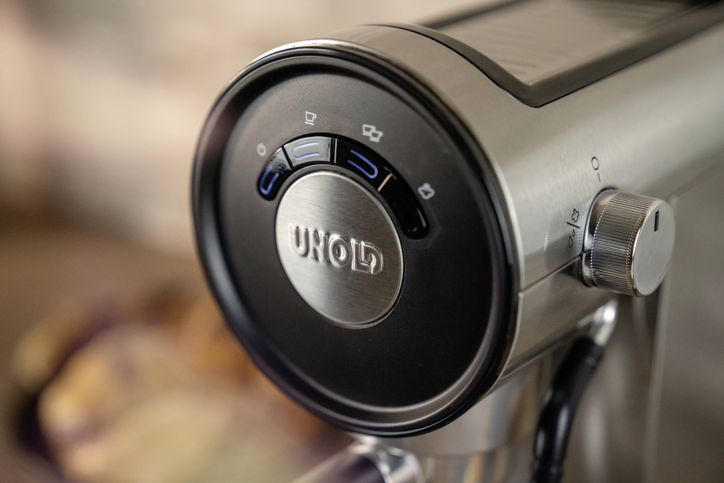 Stalowy ekspres do kawy z widocznymi przyciskami do różnych ustawień. Nazwa marki jest wyeksponowana w centrum.