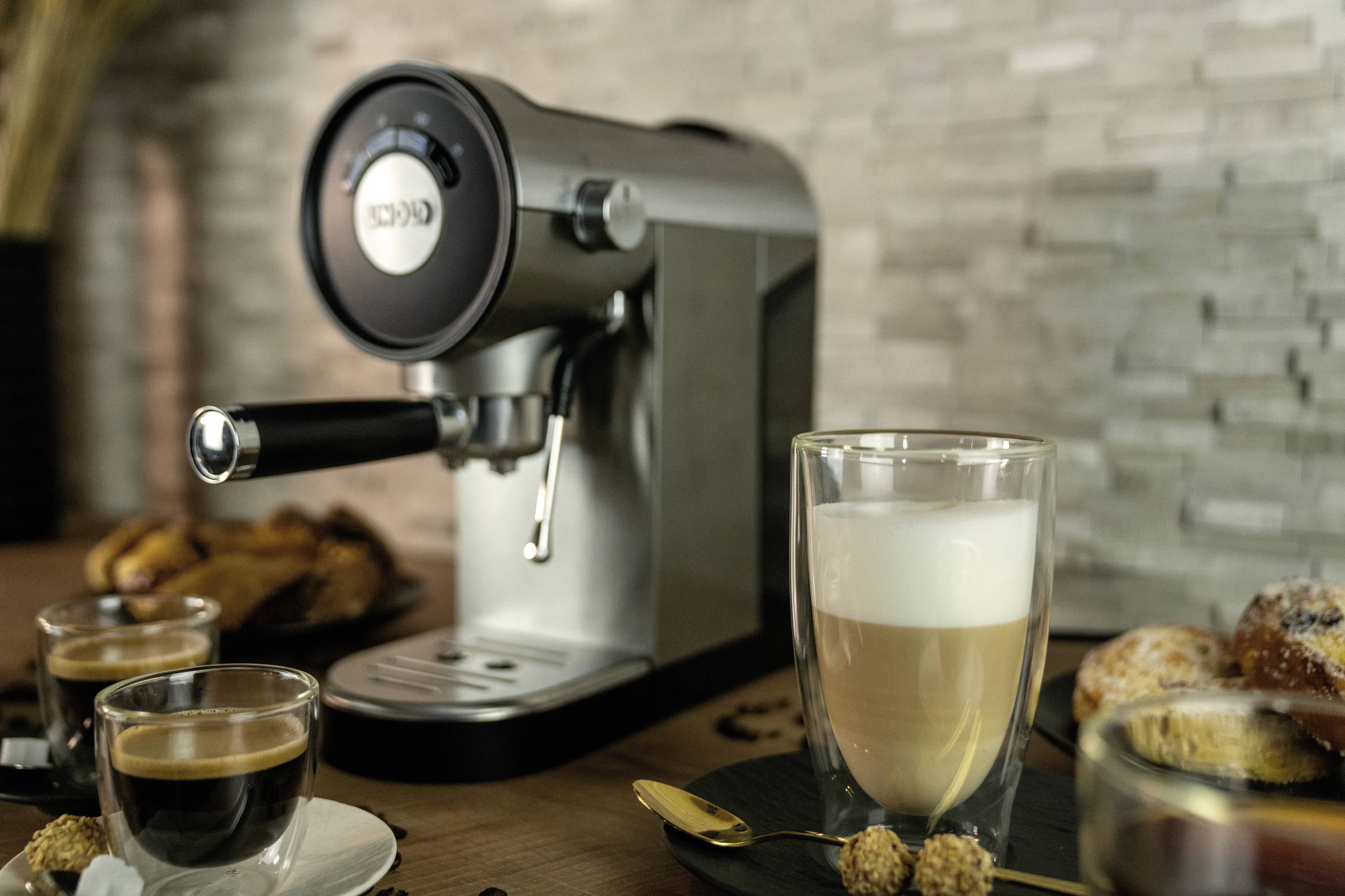 Ekspres do espresso na drewnianej powierzchni, otoczony różnymi filiżankami do kawy i wypiekami w przytulnym otoczeniu.