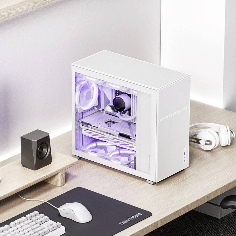 Biały komputer stacjonarny z przezroczystą ścianką boczną, przez którą widać podświetlane komponenty. Obok niego na drewnianym stole leżą słuchawki i głośnik.