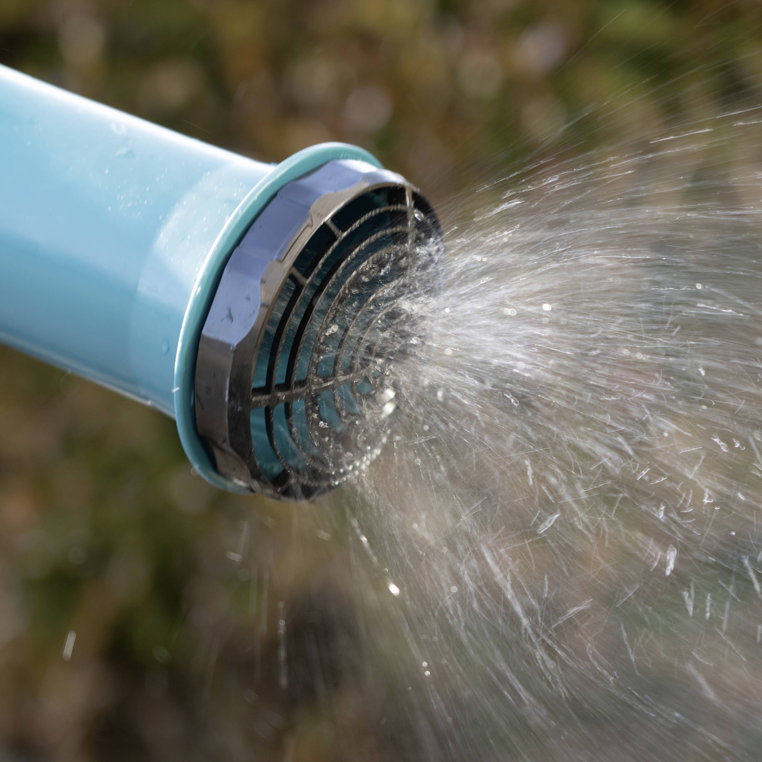 Niebieski wąż ogrodowy wystrzeliwuje strumień wody w powietrze na tle rozmytego tła, prawdopodobnie na zewnątrz.