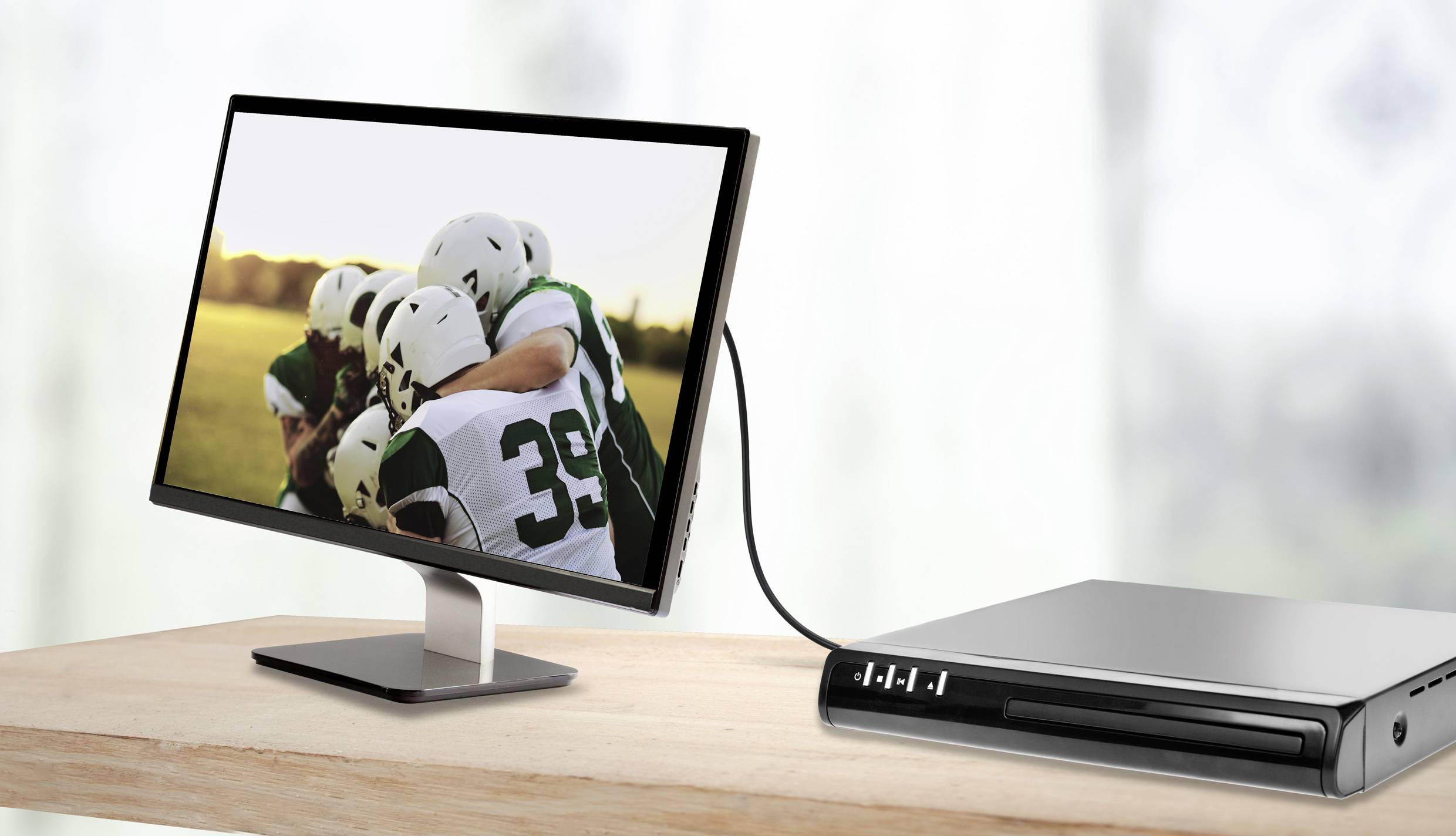 Monitor na stole wyświetla zdjęcie młodych piłkarzy w stroju sportowym, którzy się przytulają. Kabel łączy monitor z odtwarzaczem.