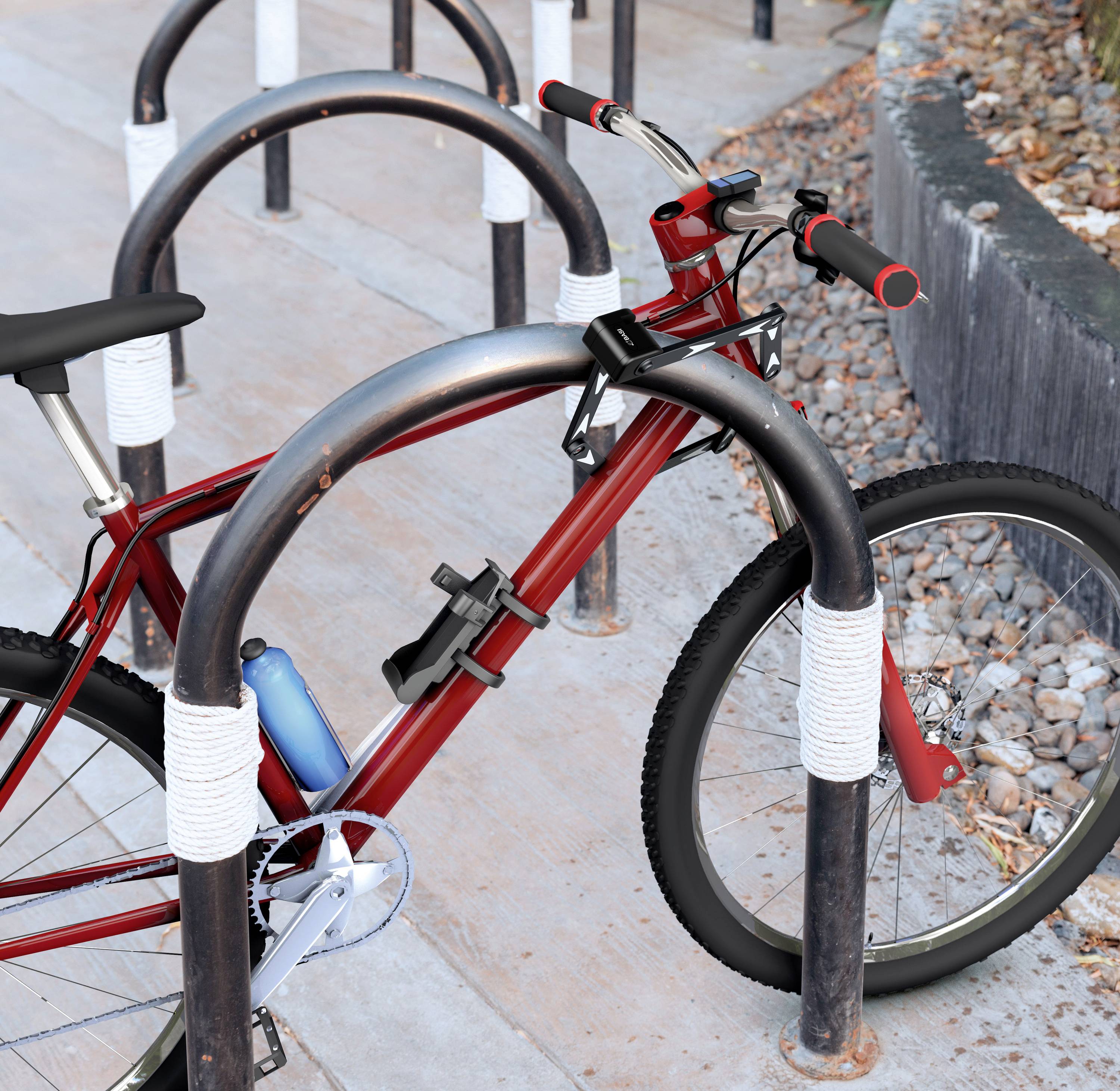 Czerwony rower jest przypięty do stojaka rowerowego w miejskim otoczeniu. Widoczny jest szary chodnik i kamienie.