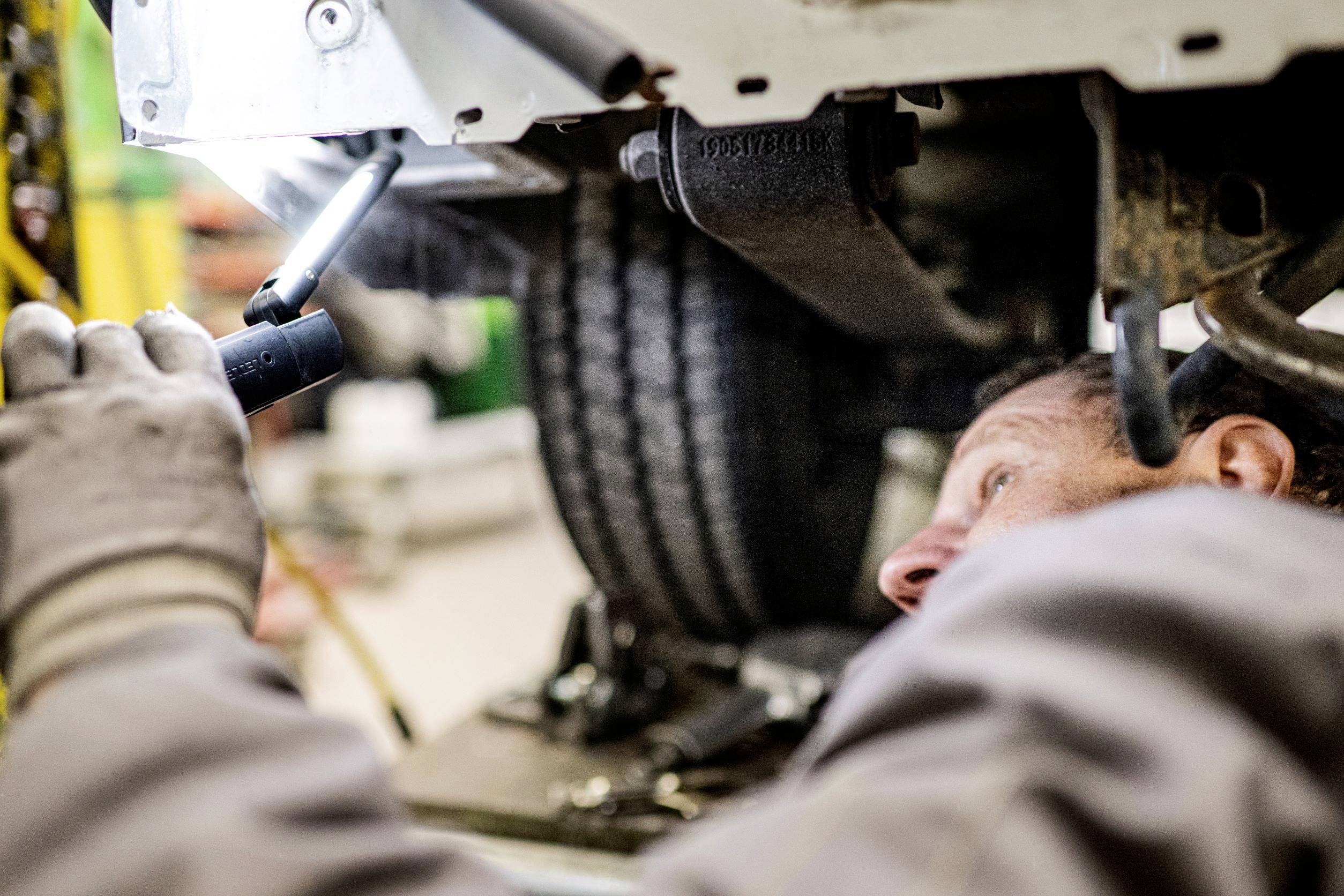 Mechanik przygląda się podwoziu pojazdu za pomocą latarki. Widoczne są szczegóły zawieszenia i narzędzi.