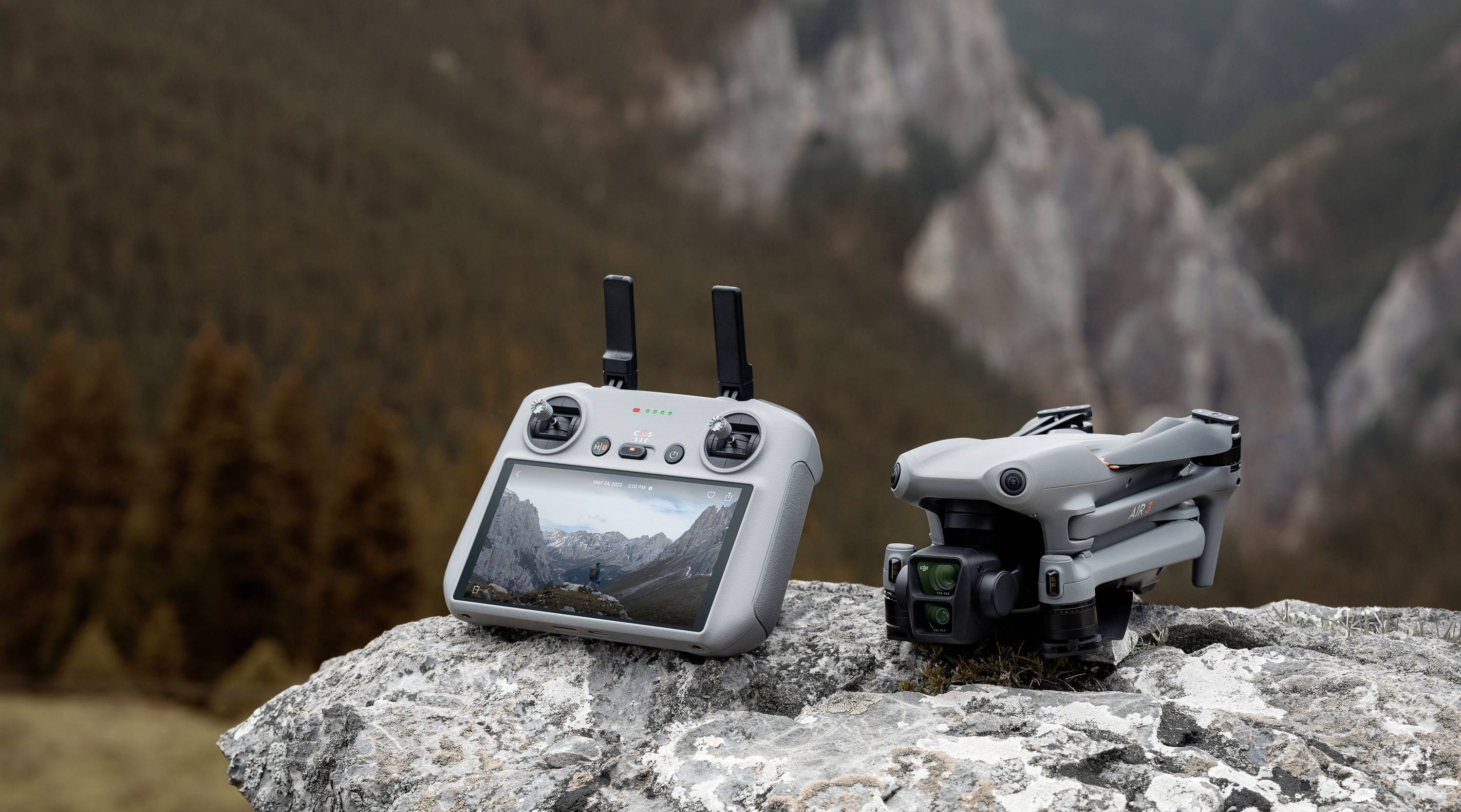 Dron i pilot zdalnego sterowania z wyświetlaczem prezentują krajobraz górski. Leżą na skale w zalesionym otoczeniu.