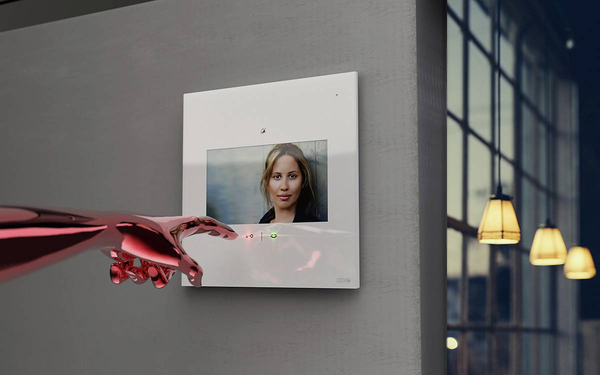 Cyfrowa ramka na zdjęcia wyświetla portret kobiety na ścianie. Metalowa ręka dotyka ramki. W tle widoczne są żaluzje okienne.