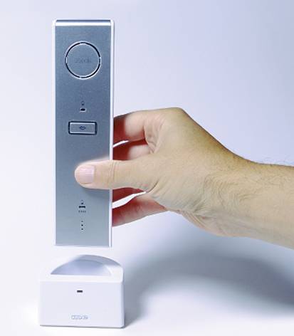 Dłoń trzyma srebrny, podłużny telefon wsadzony do białej stacji ładującej. Telefon został zaprojektowany w minimalistycznym stylu.