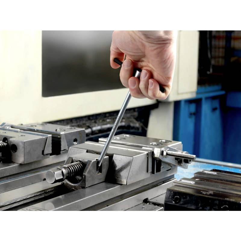 Ręka mocuje przedmiot obróbki kluczem w imadłach maszynowych, przygotowując go do procesu obróbki.