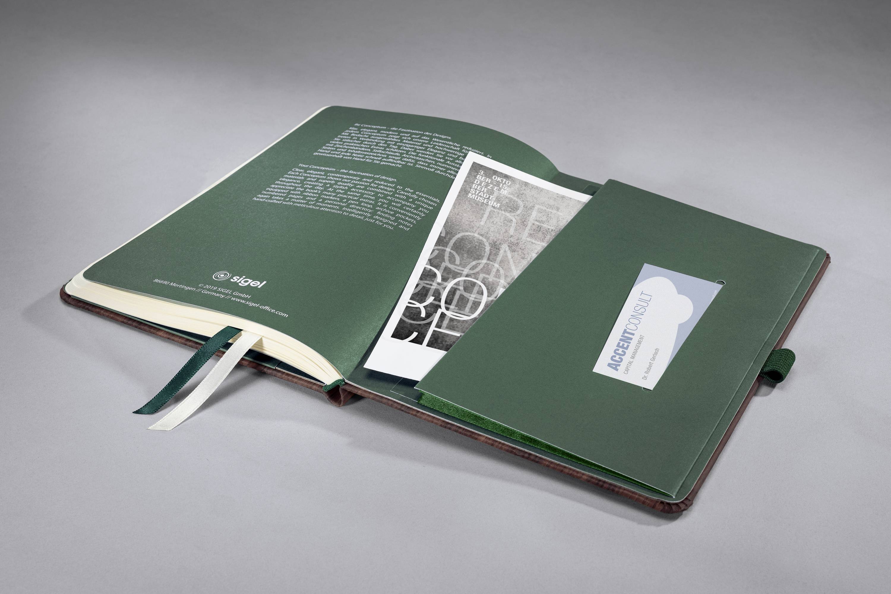 Otwarty notes z zielonymi okładkami, przedstawiający stronę tekstową oraz kieszeń po prawej stronie, w której znajdują się dokument i wizytówka.