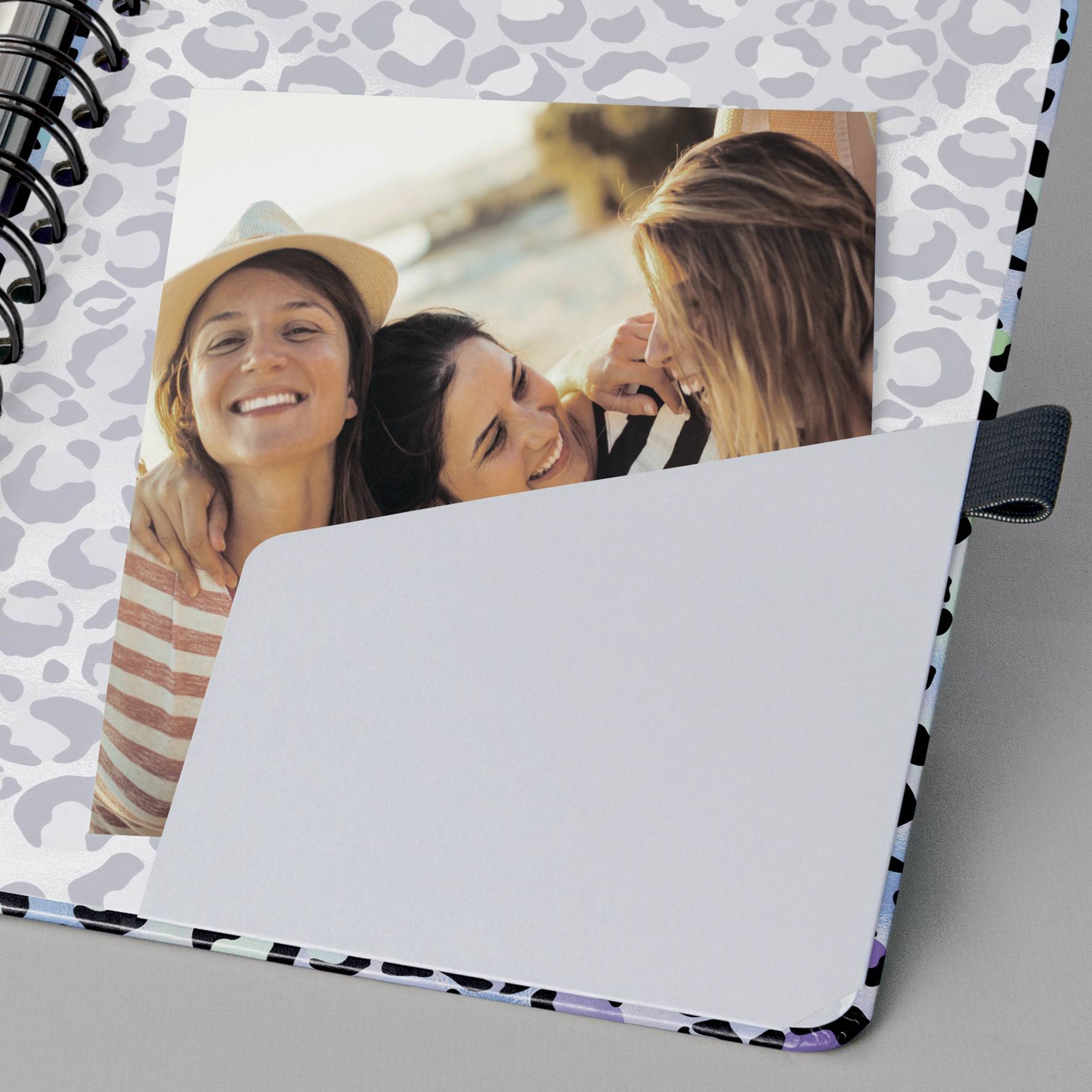 Trzy uśmiechnięte kobiety robią sobie selfie na plaży. Jedna z nich ma na głowie kapelusz. Zdjęcie jest przypięte do zeszytu w panterkę.