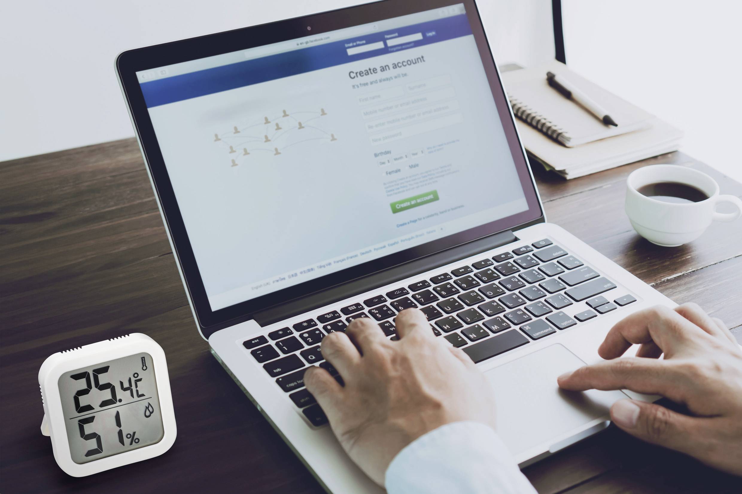 Osoba pisze na laptopie wyświetlającym stronę logowania. Obok znajduje się termohigrometr wskazujący temperaturę 25,4°C i wilgotność powietrza 51%.