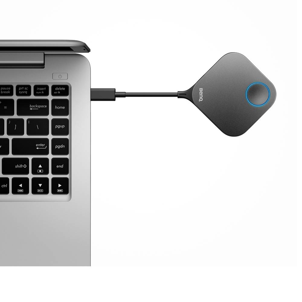 Laptop z podłączonym donglem ClickShare. Dongle wyświetla niebieską diodę statusową i jest przeznaczony do bezprzewodowych prezentacji.