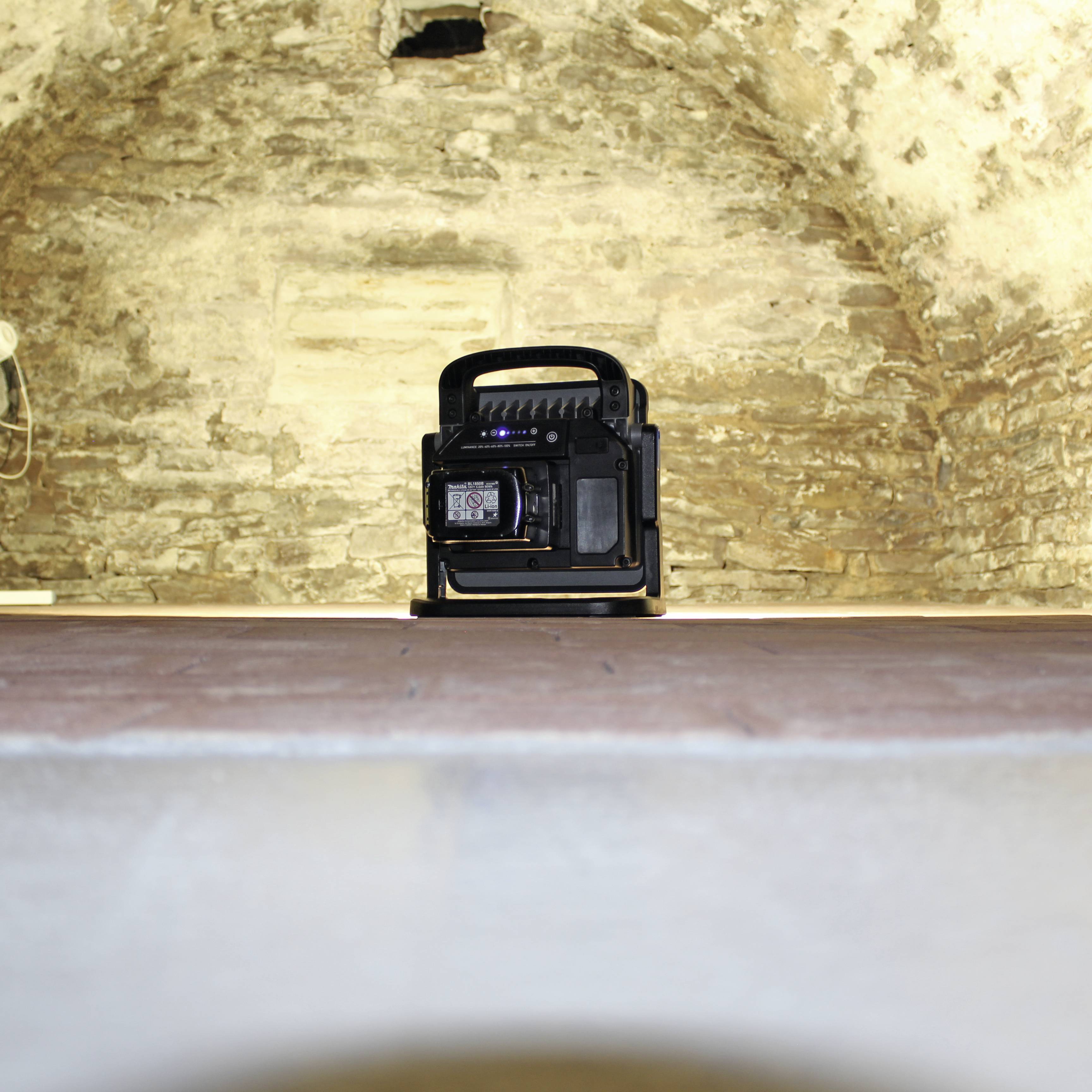 Przenośna gazowa grzejka stoi na płaskiej powierzchni w pomieszczeniu o solidnych kamiennych ścianach.