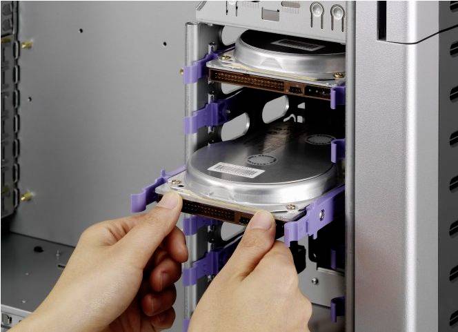 Osoba instaluje dysk twardy w obudowie komputera. Ręce trzymają dysk twardy, który jest wsuwany do wnęki na nośniki.