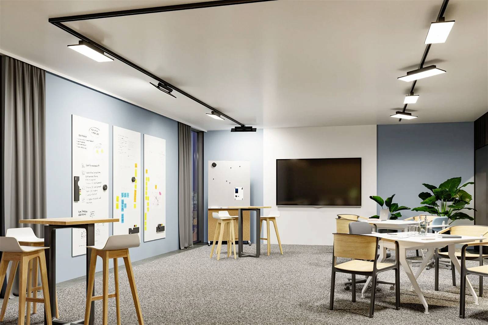 Nowoczesna sala konferencyjna z jasnymi ścianami, stołami, krzesłami, tablicami whiteboard i dużym ekranem. Rośliny w rogu pomieszczenia.