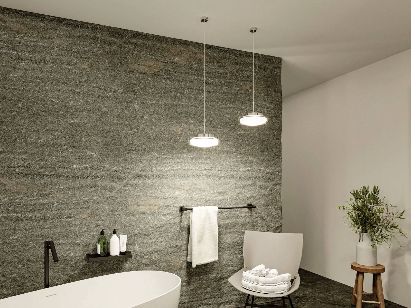 Łazienka z wolnostojącą wanną, dwiema wiszącymi lampami i kamienną ścianą. Przy niej stoi krzesło z ułożonymi ręcznikami.