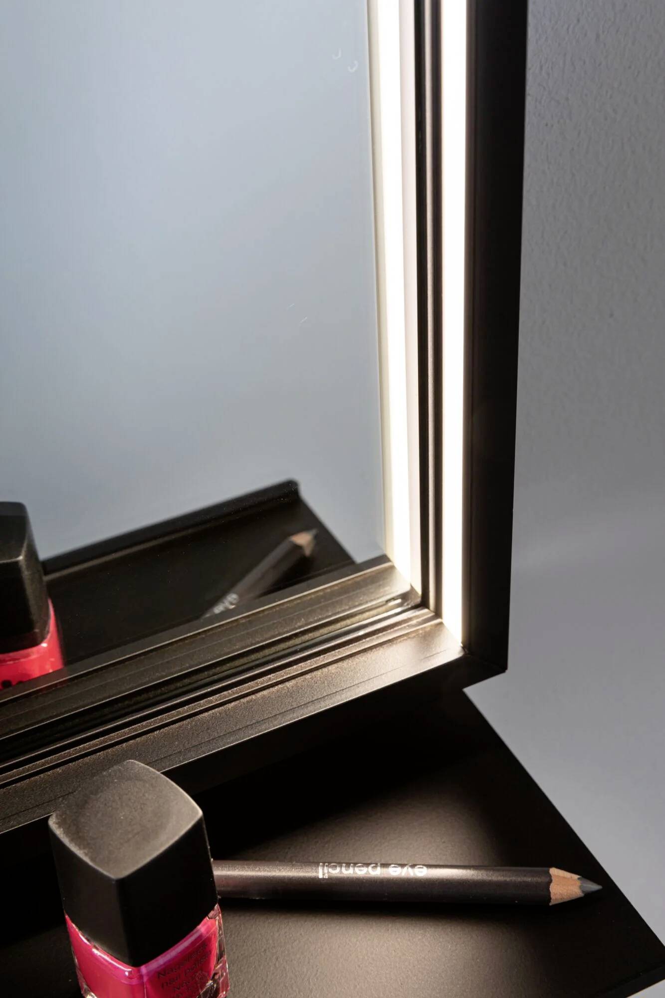 Podświetlone lustro kosmetyczne obok szminki i kredki do oczu na czarnej powierzchni.